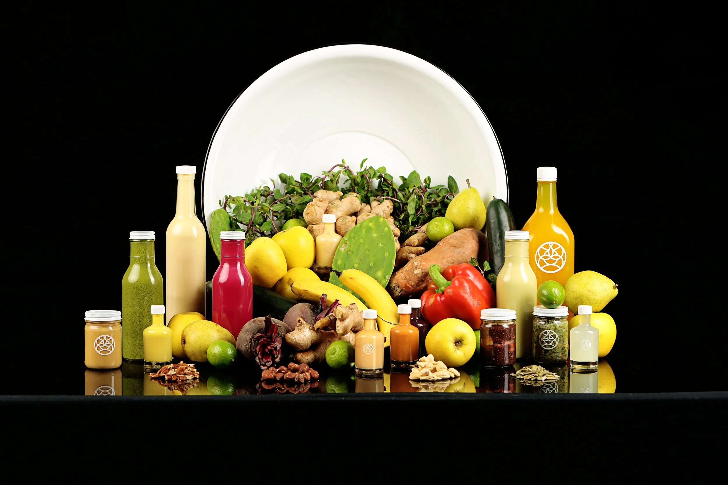 Assorted fresh fruits, vegetables, herbs, spices, and bottles of colorful liquids on a black background.