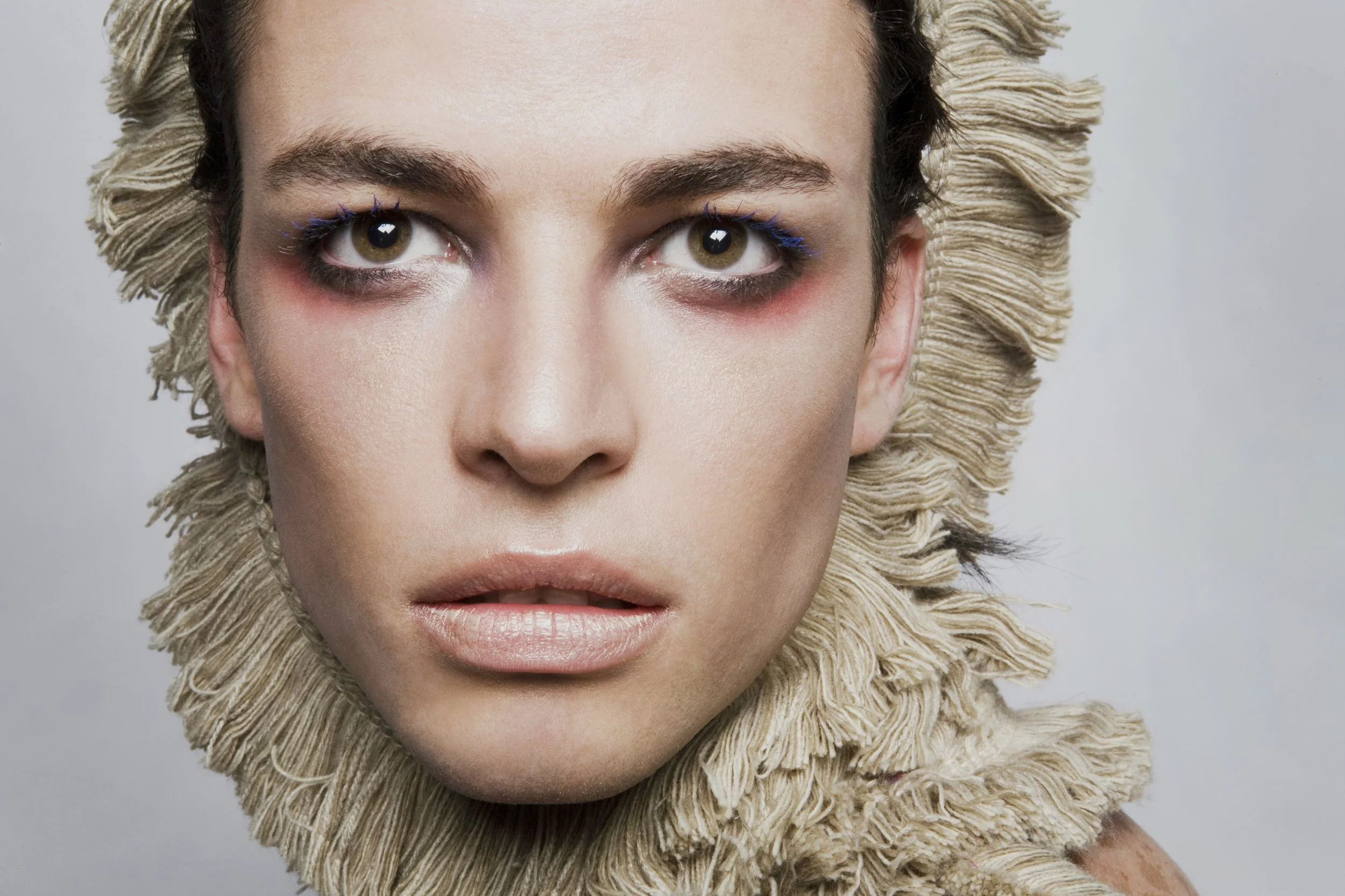 Close-up of a woman with styled hair and makeup, wearing a textured, possibly fur-lined, garment.