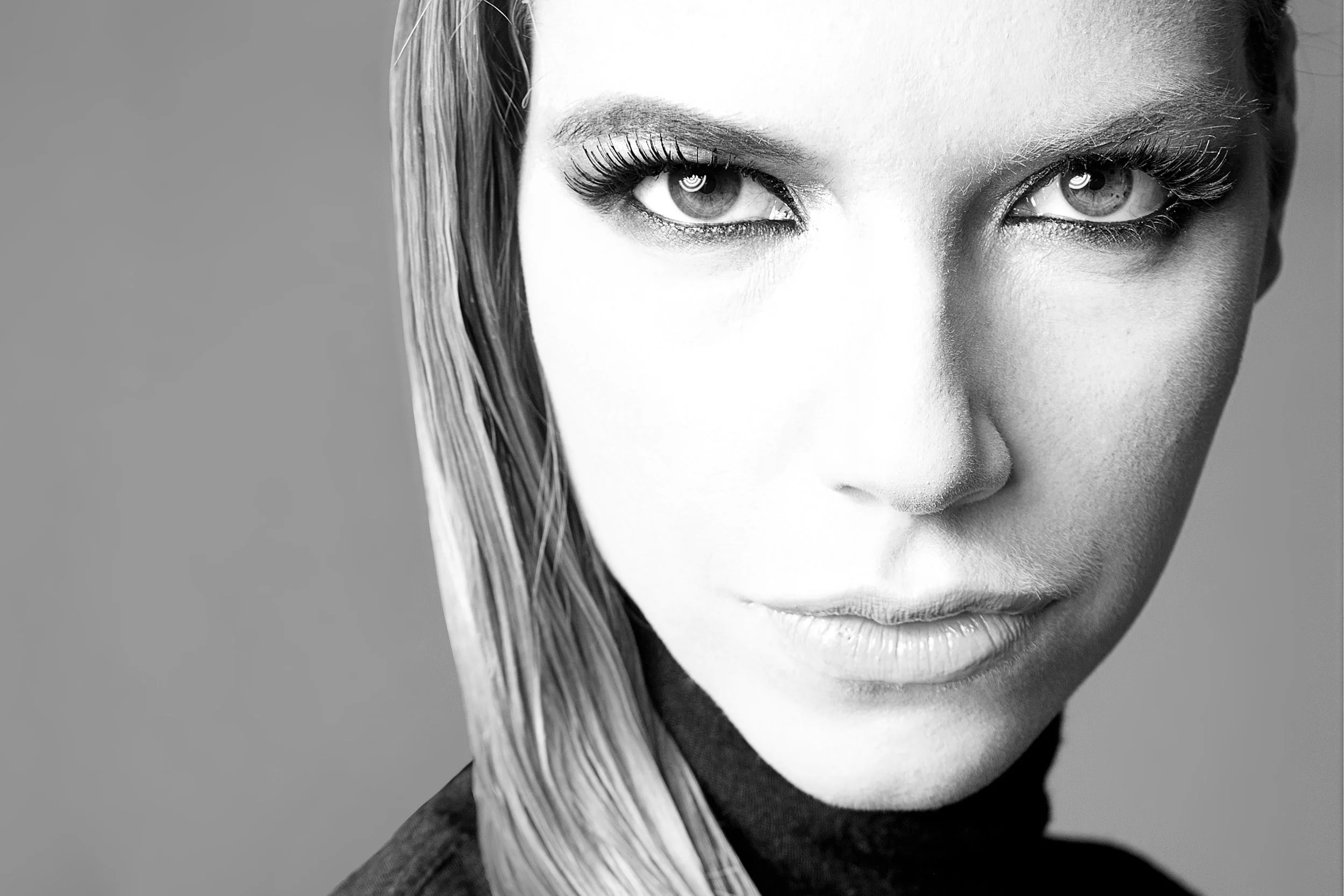 Close-up black and white photo of a woman's face showing only part of her face and hair. She has bright eyes and long lashes, with some wet hair strands hanging down.