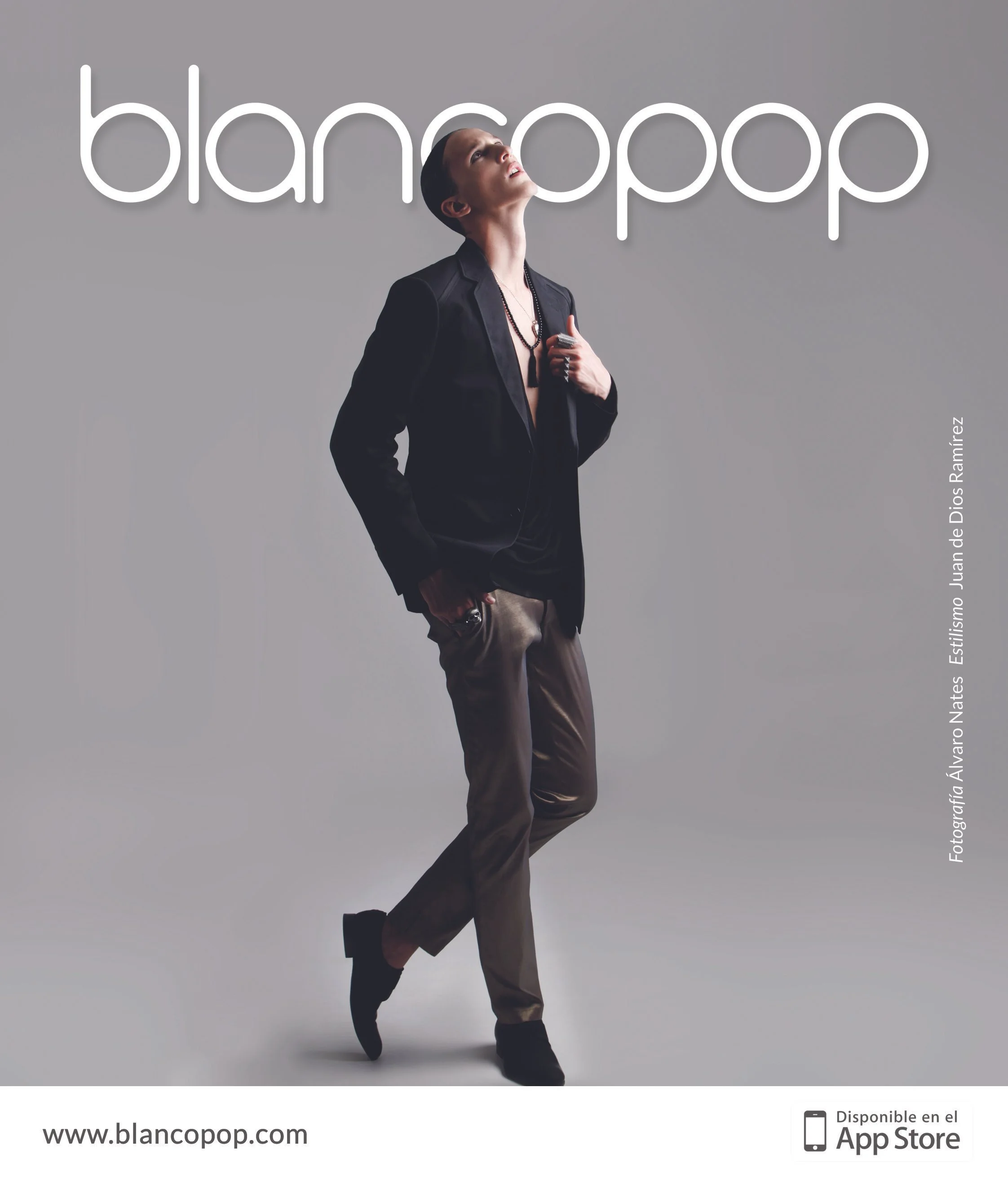 A person with short dark hair, wearing a black blazer, beige pants, and black boots, stands against a plain gray background. They have a rings and necklace, looking upward with a thoughtful expression. Neon-style white text behind them reads 'blancop
