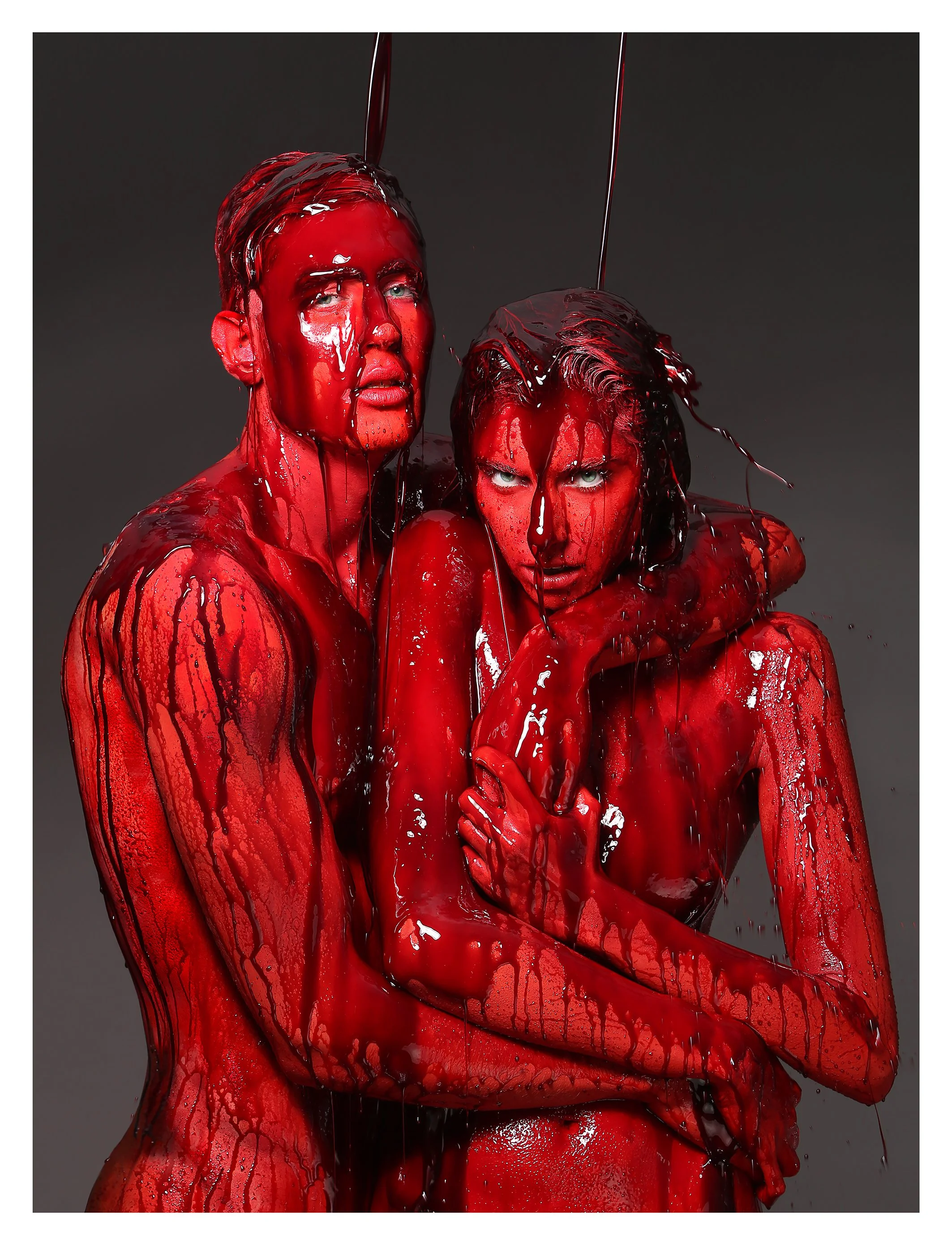 A person covered in red liquid, with their hair and face dripping. They are looking directly at the camera, and the background is dark gray.
