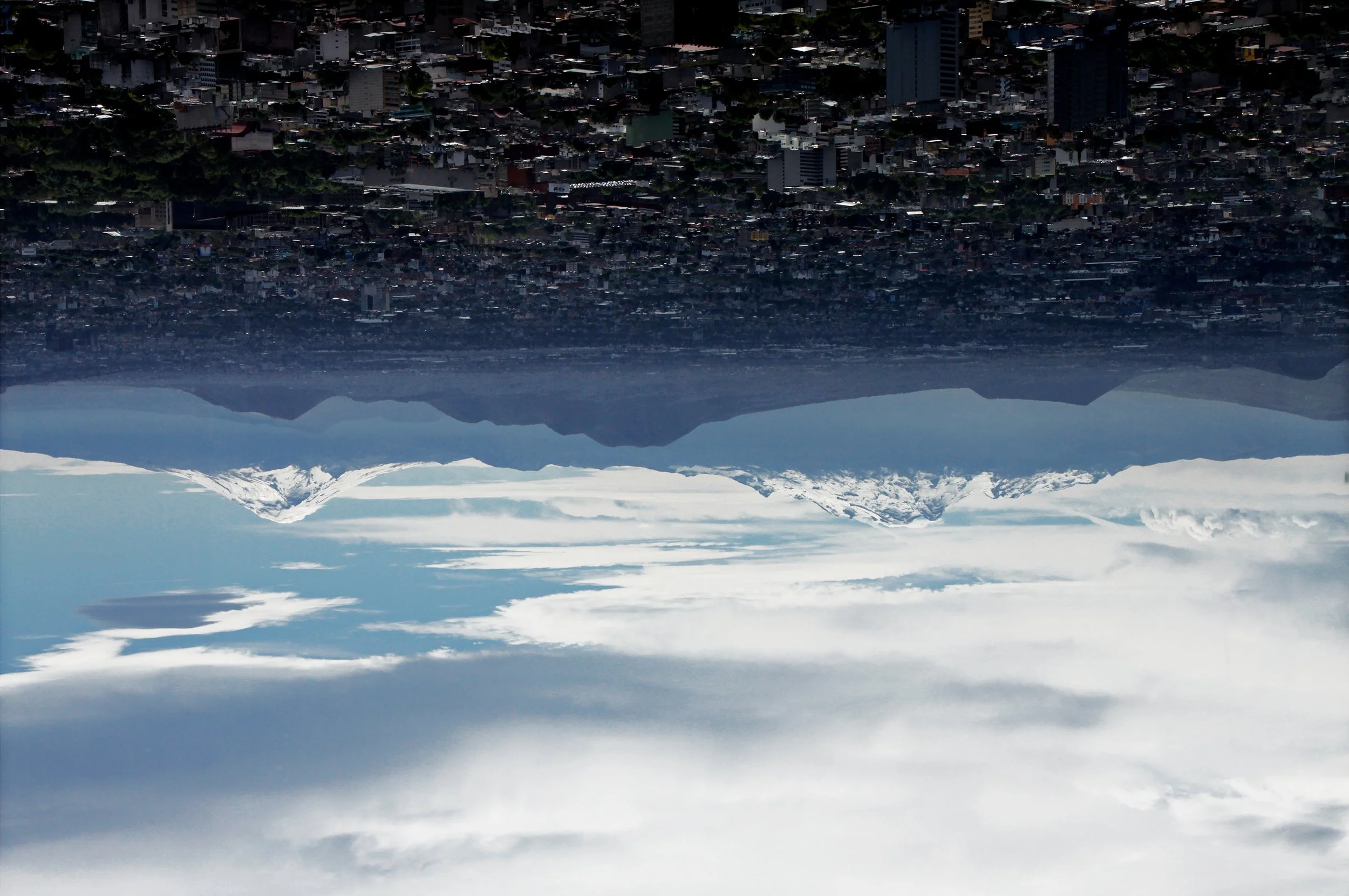 Upside down cityscape with mountains in the background, snowy peaks visible and clouds in the sky.
