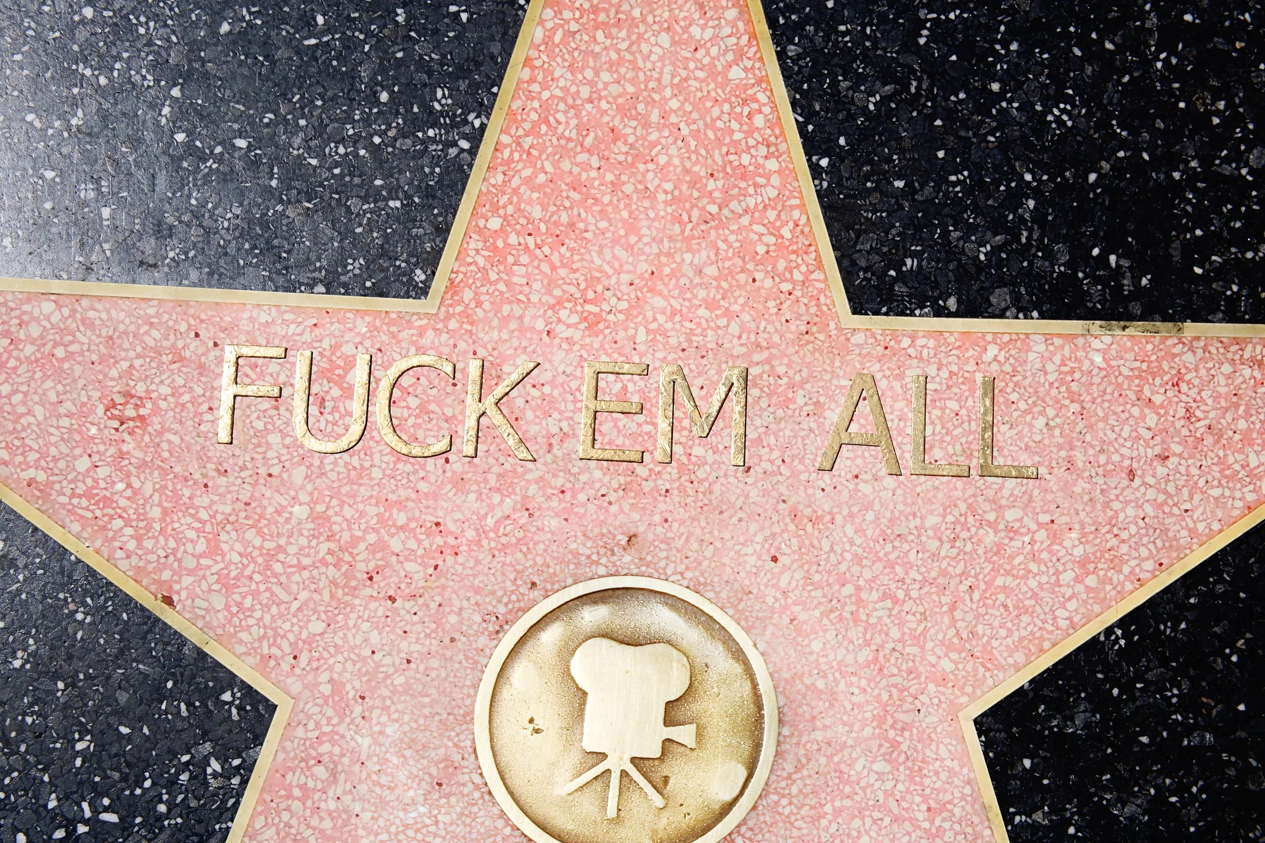 A star on the Hollywood Walk of Fame with the phrase 'FUCK EM ALL' engraved on it, and a small emblem with a man's silhouette and ramen noodles.