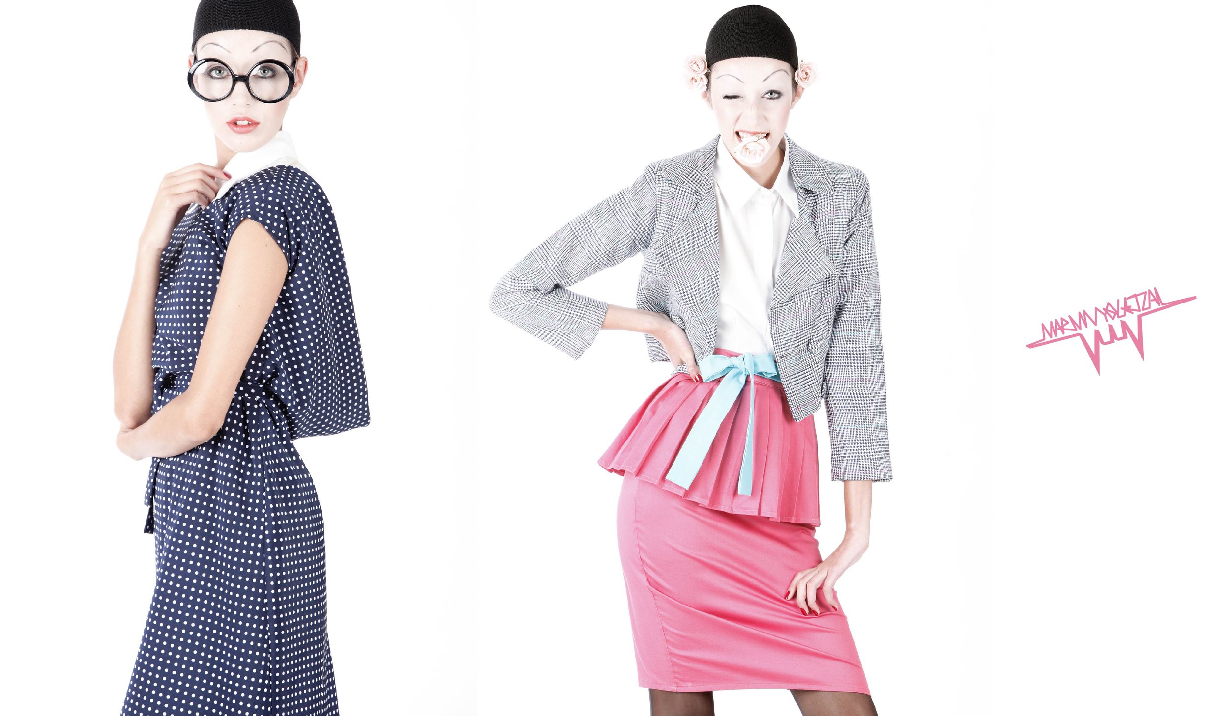 Two women dressed in vintage-style clothing with bold makeup and black beanies, posing against a plain white background. The woman on the left is wearing glasses and a polka dot dress, while the woman on the right is in a plaid blazer and pink skirt 