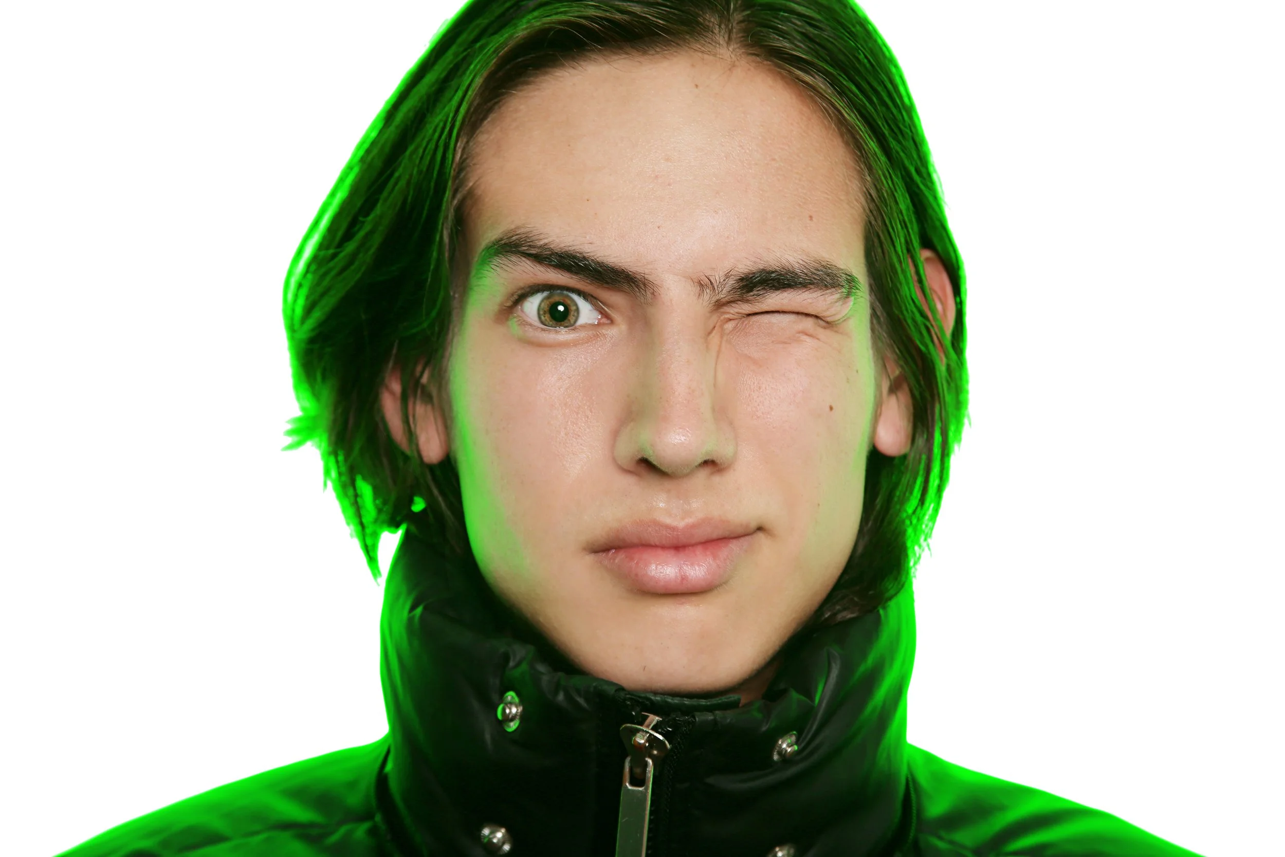Close-up of a woman with short black hair, one eye winking, wearing a black jacket with metal buttons, outlined with a green glow.