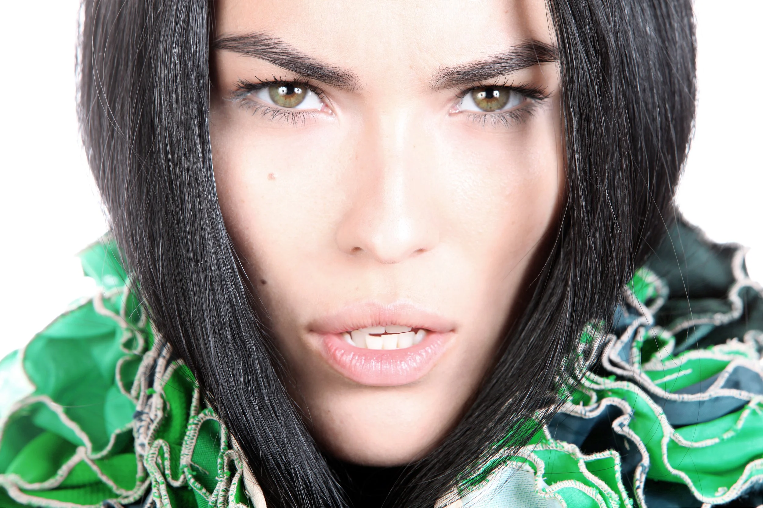Close-up of a woman with dark hair, hazel eyes, and light skin, wearing a green patterned hoodie.