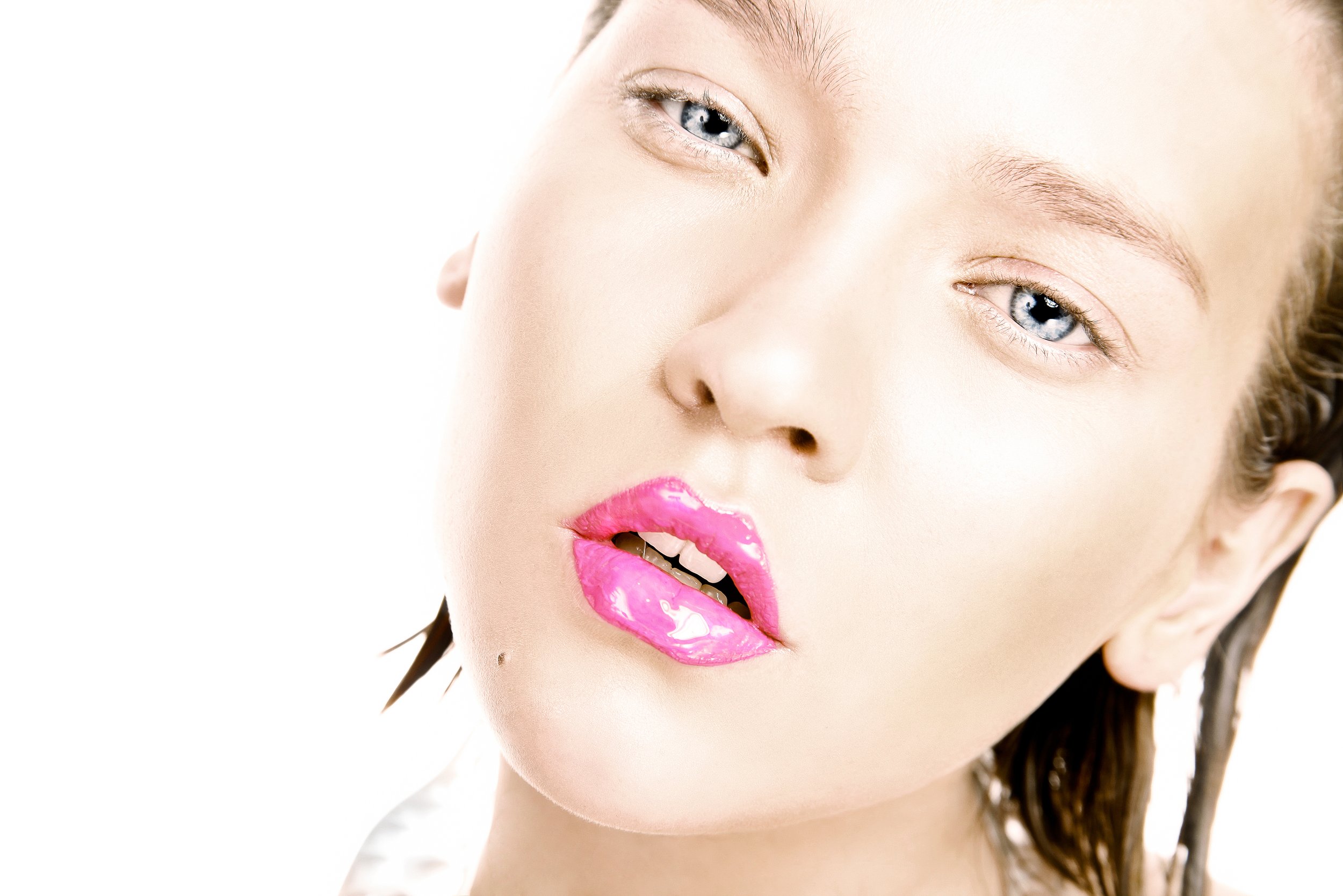 A close-up of a woman with painted pink lips, blue eyes, and light makeup, in a glamorous pose.