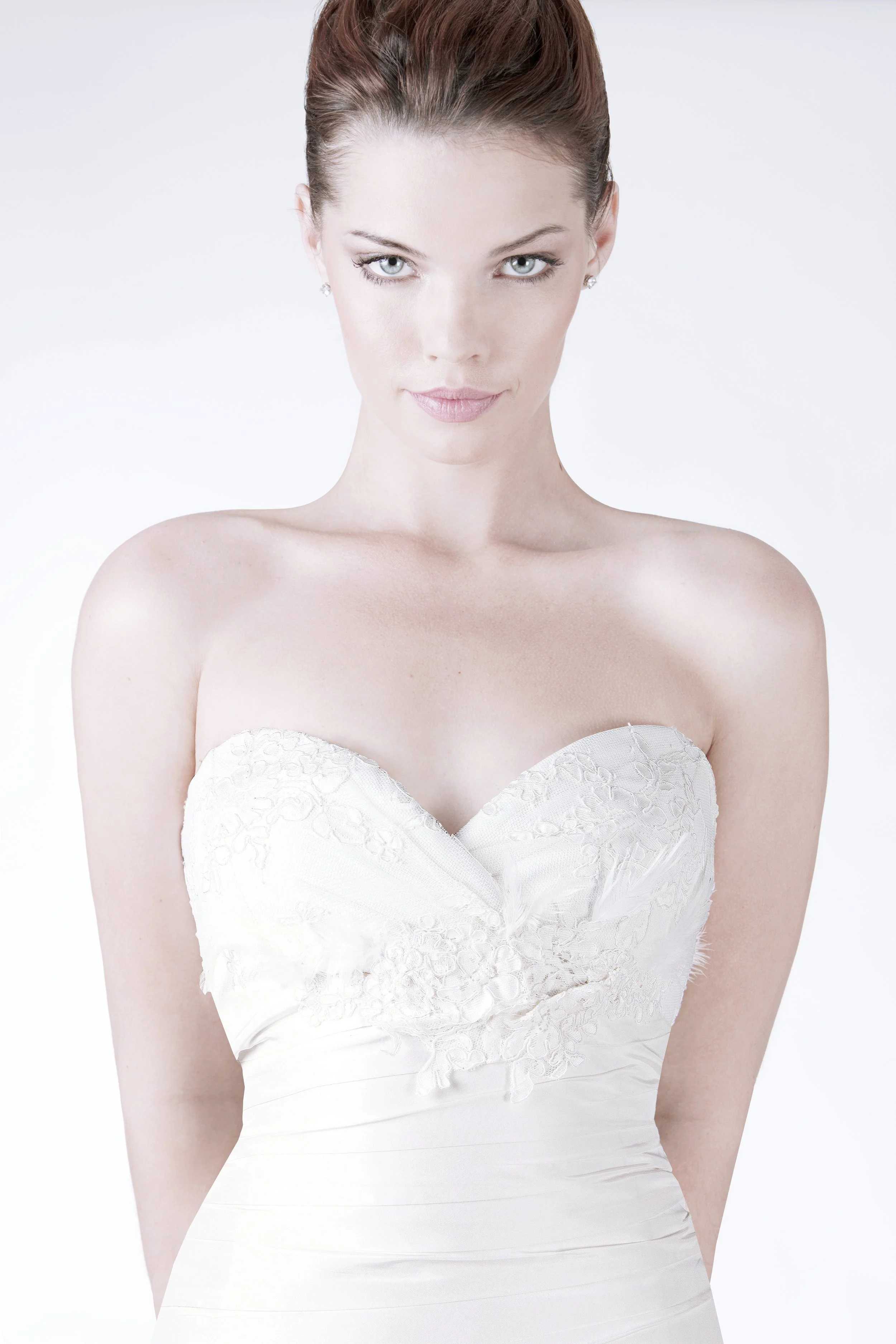 A woman with fair skin and green eyes wearing a white strapless wedding dress with lace details, posing against a plain white background.