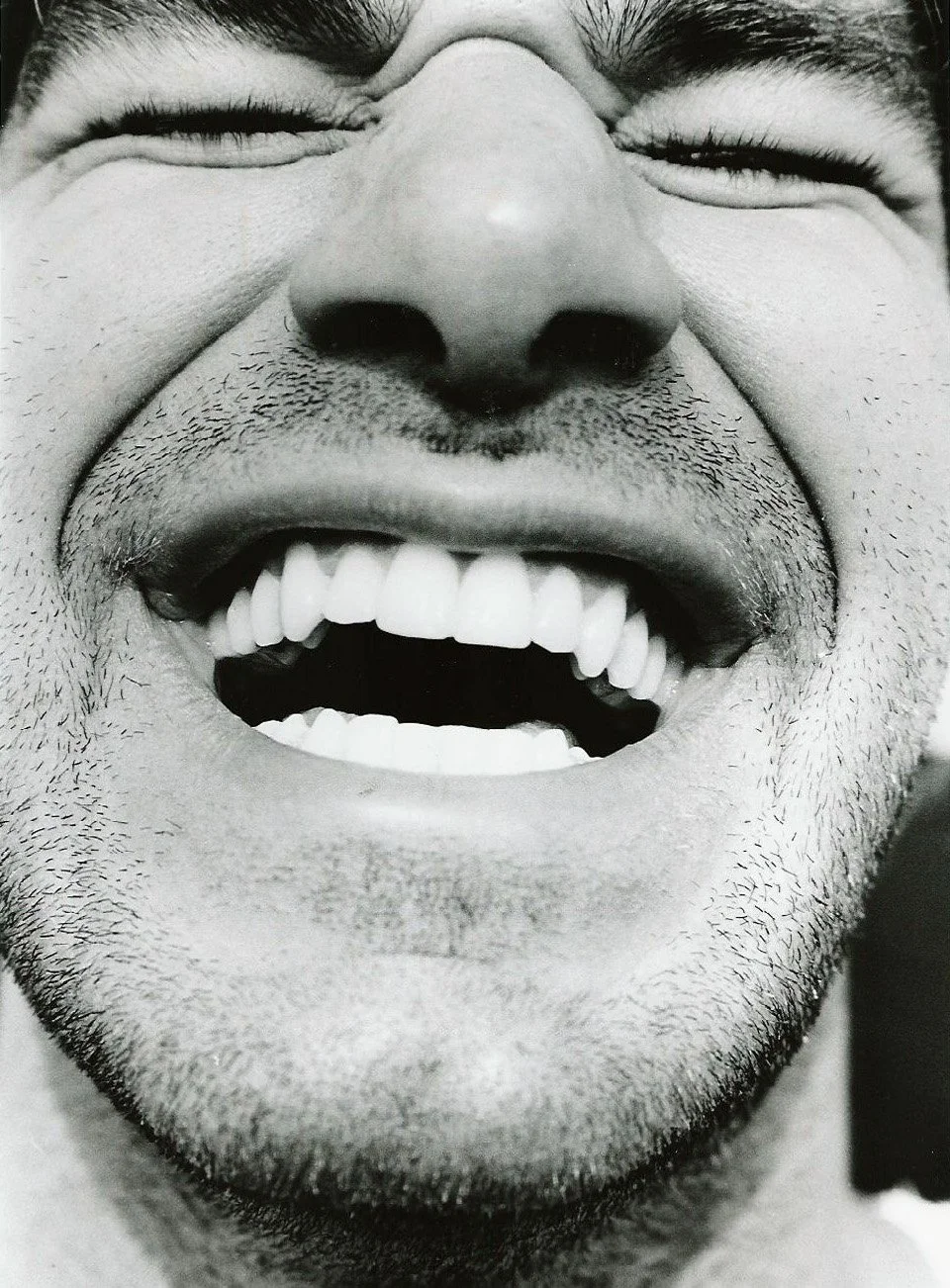 Close-up of a person's face smiling widely, showing teeth and some facial hair