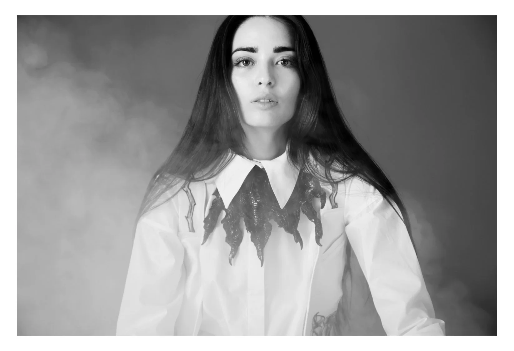 Black and white portrait of a woman with long dark hair, wearing a white shirt with a distinctive collar and dark decorative elements near the collar.