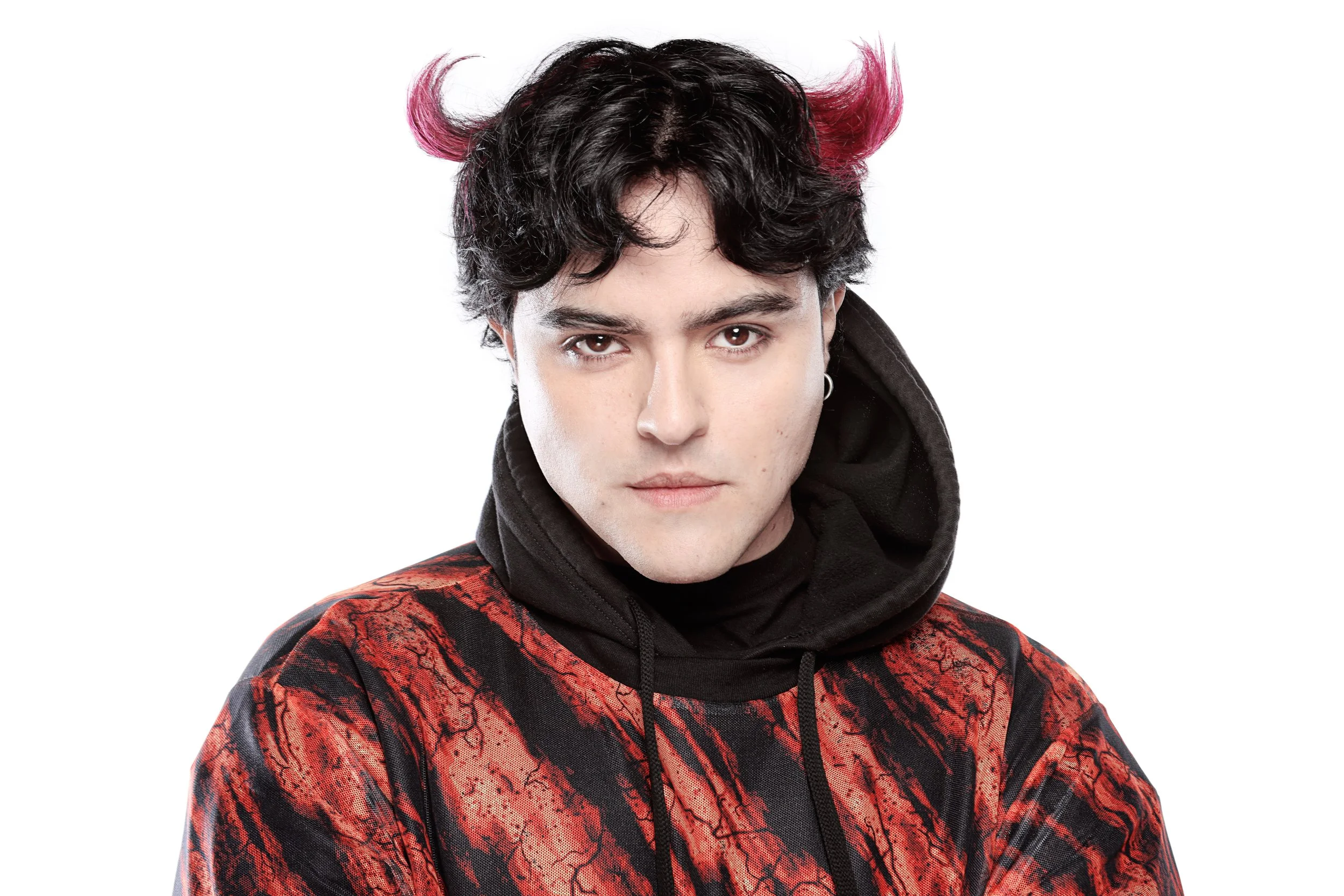 A young man with black and pink hair, wearing a black and red hoodie, looking directly at the camera against a white background.