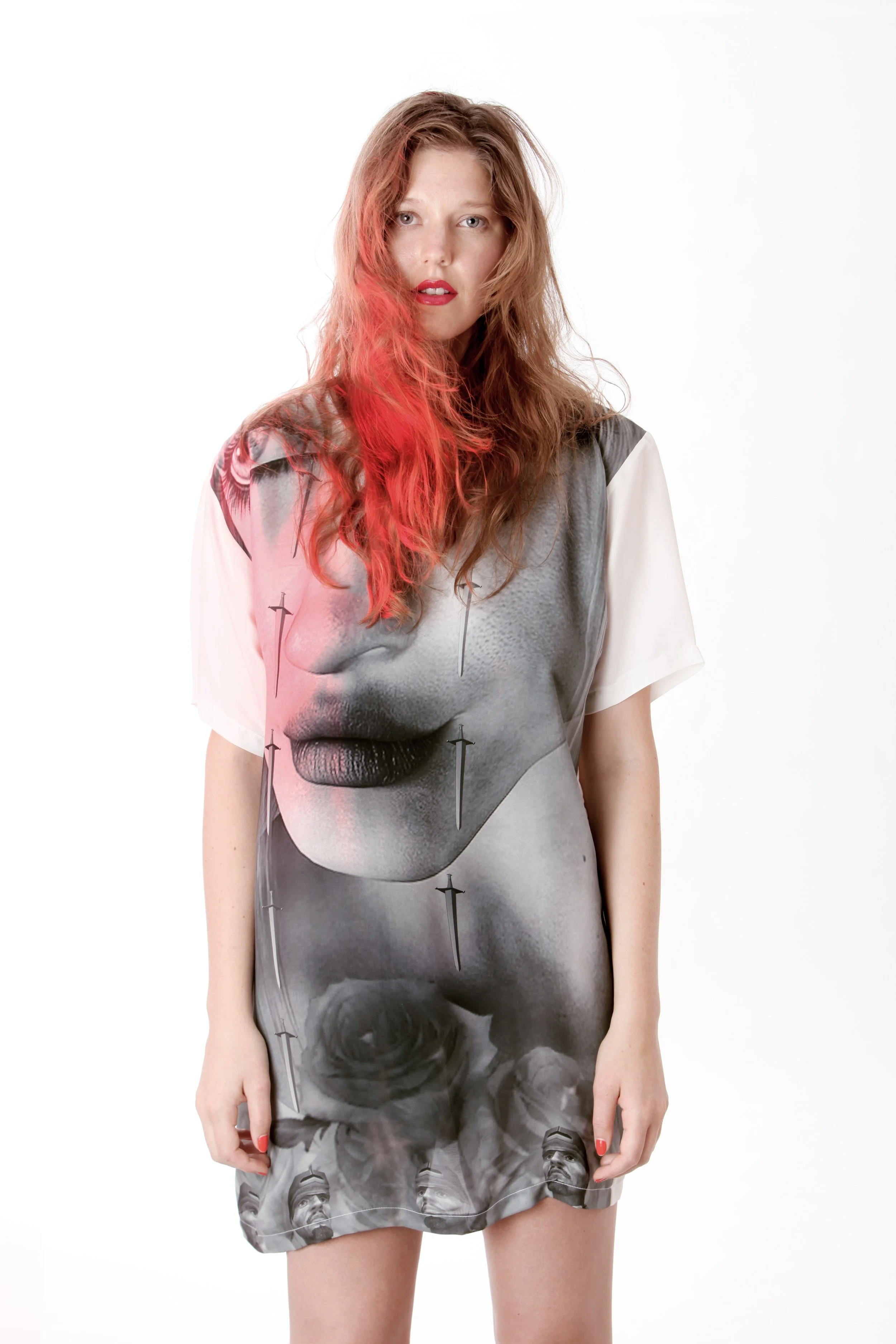 A woman with long red hair and red lipstick wearing a dress featuring a black and white photographic print of a woman's face, black roses, and small images of African American men with a beard and hat.