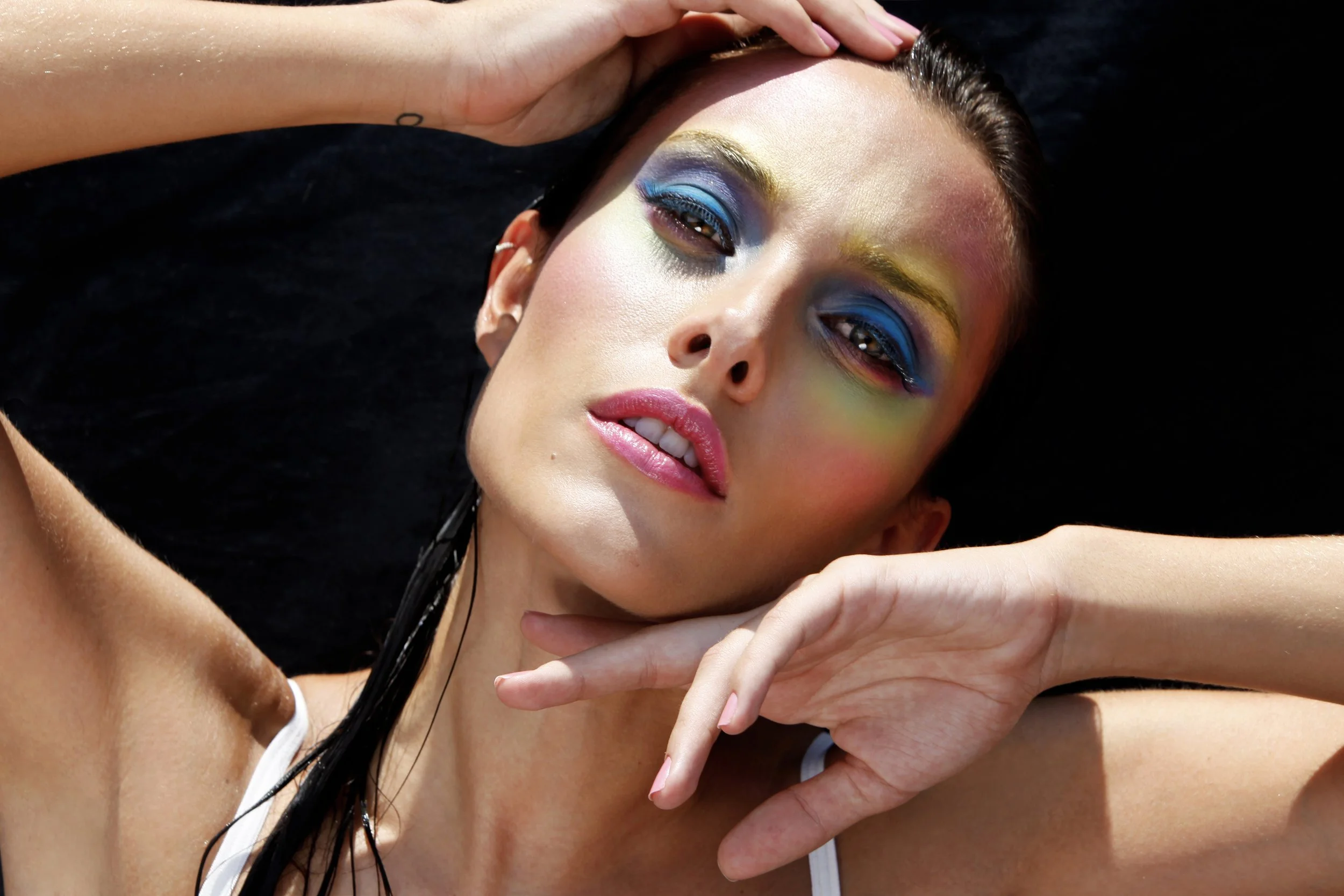 A woman with vibrant, colorful eye makeup lying down with her eyes closed.