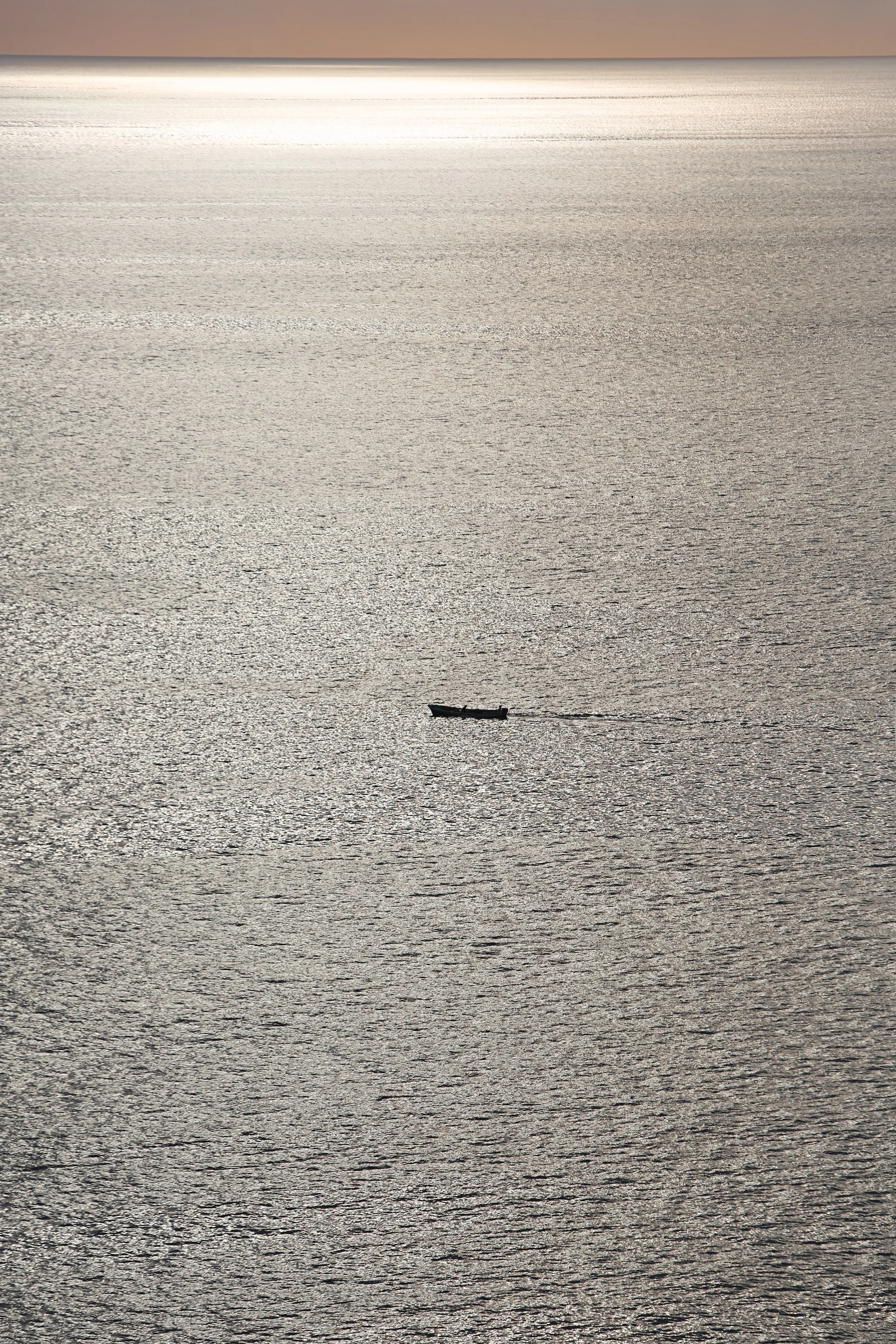 A boat cruising on a calm, reflective body of water during sunset with a haze in the sky.