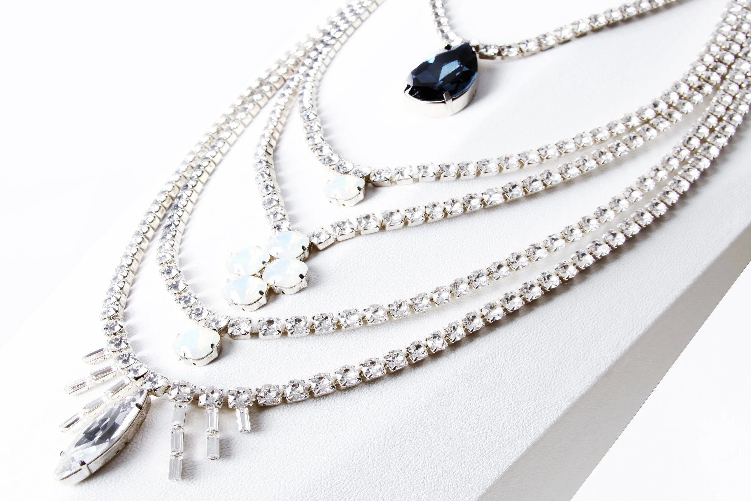 Multiple sparkling diamond necklaces with different designs laid out on a white surface, featuring a large black gemstone pendant.