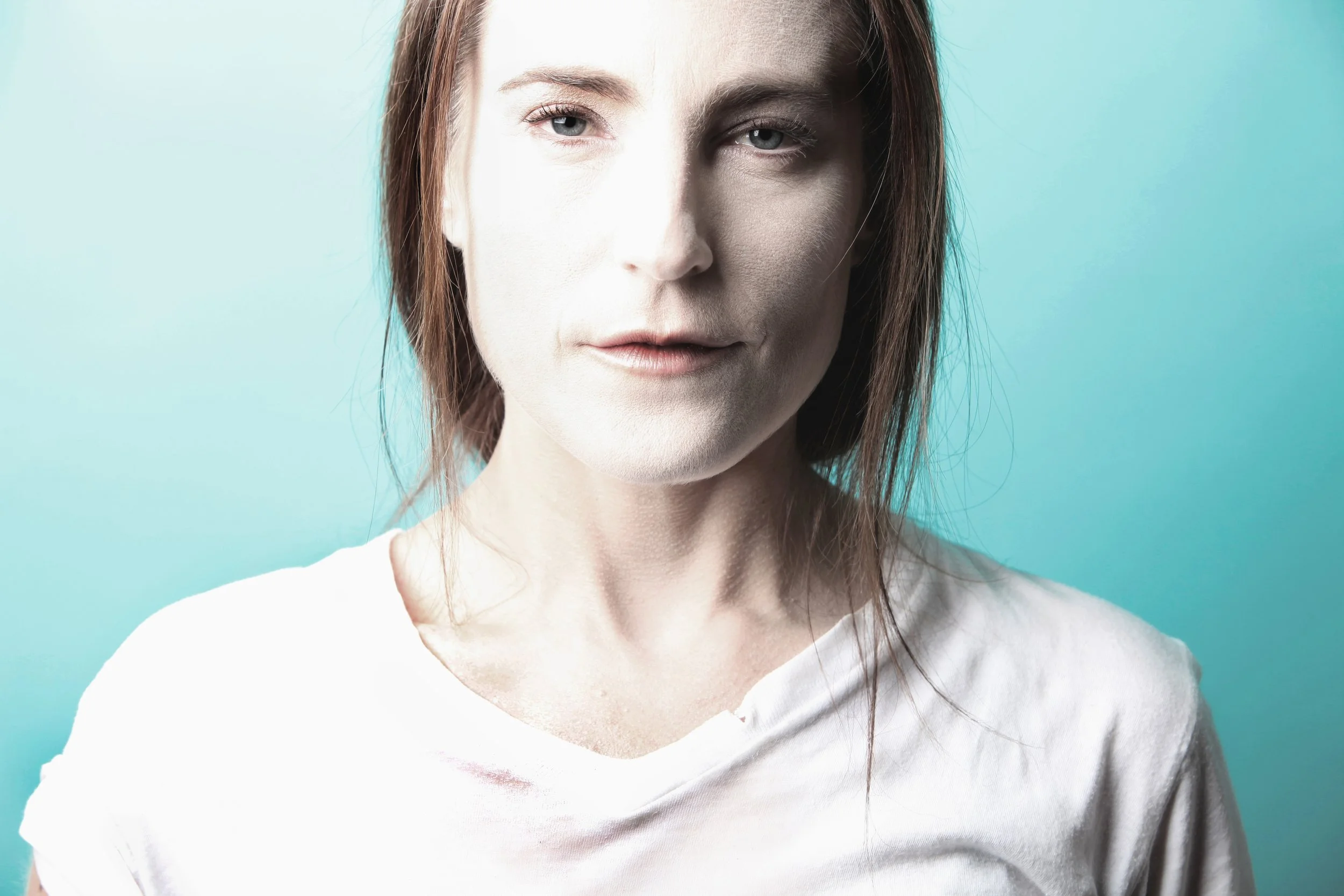 Close-up of a woman with half her face brightly lit and the other half in shadow against a teal background.