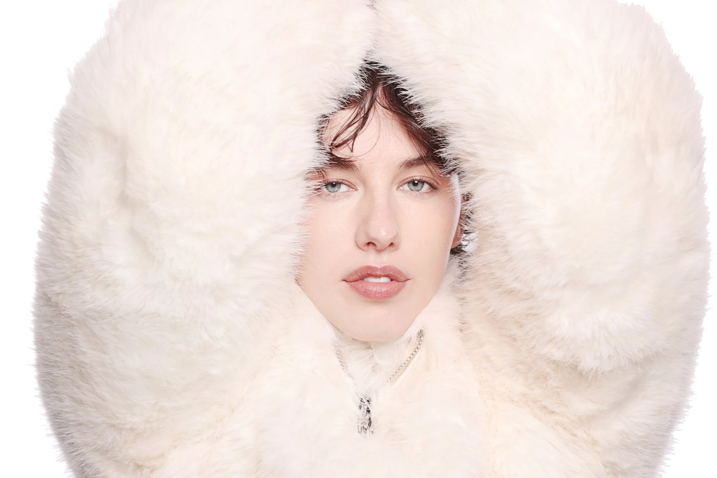 A woman with blue eyes and wet hair surrounded by a thick, white, fluffy fur coat or scarf.