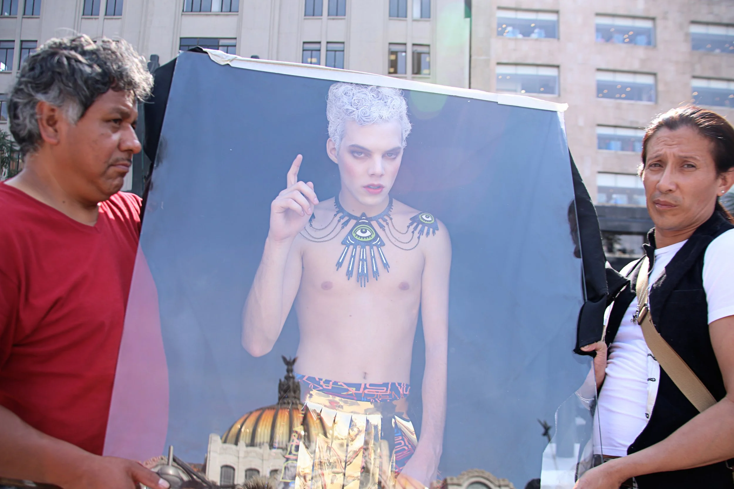 Two people holding a reflective poster of a woman with curly gray hair and fantasy-style jewelry