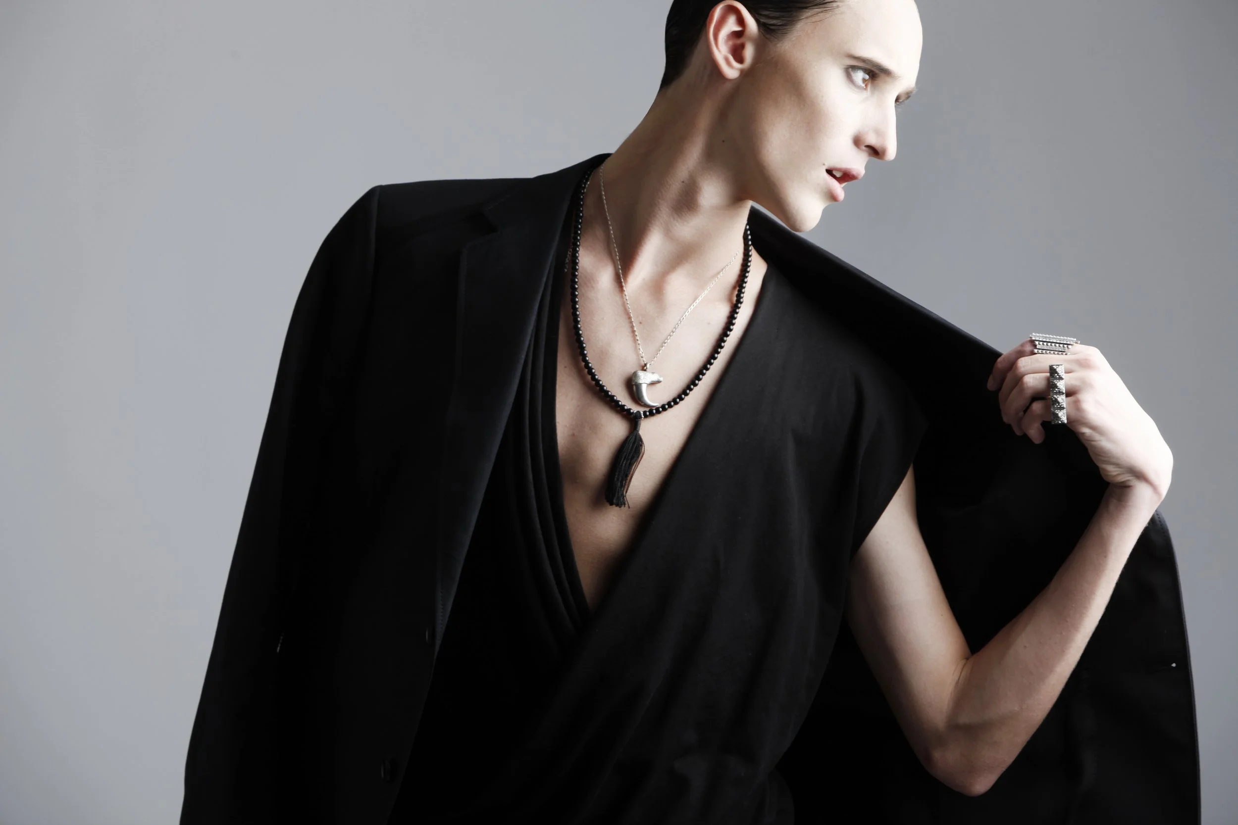 A woman with short dark hair wearing a black blazer and jewelry, holding a ring, against a neutral background.