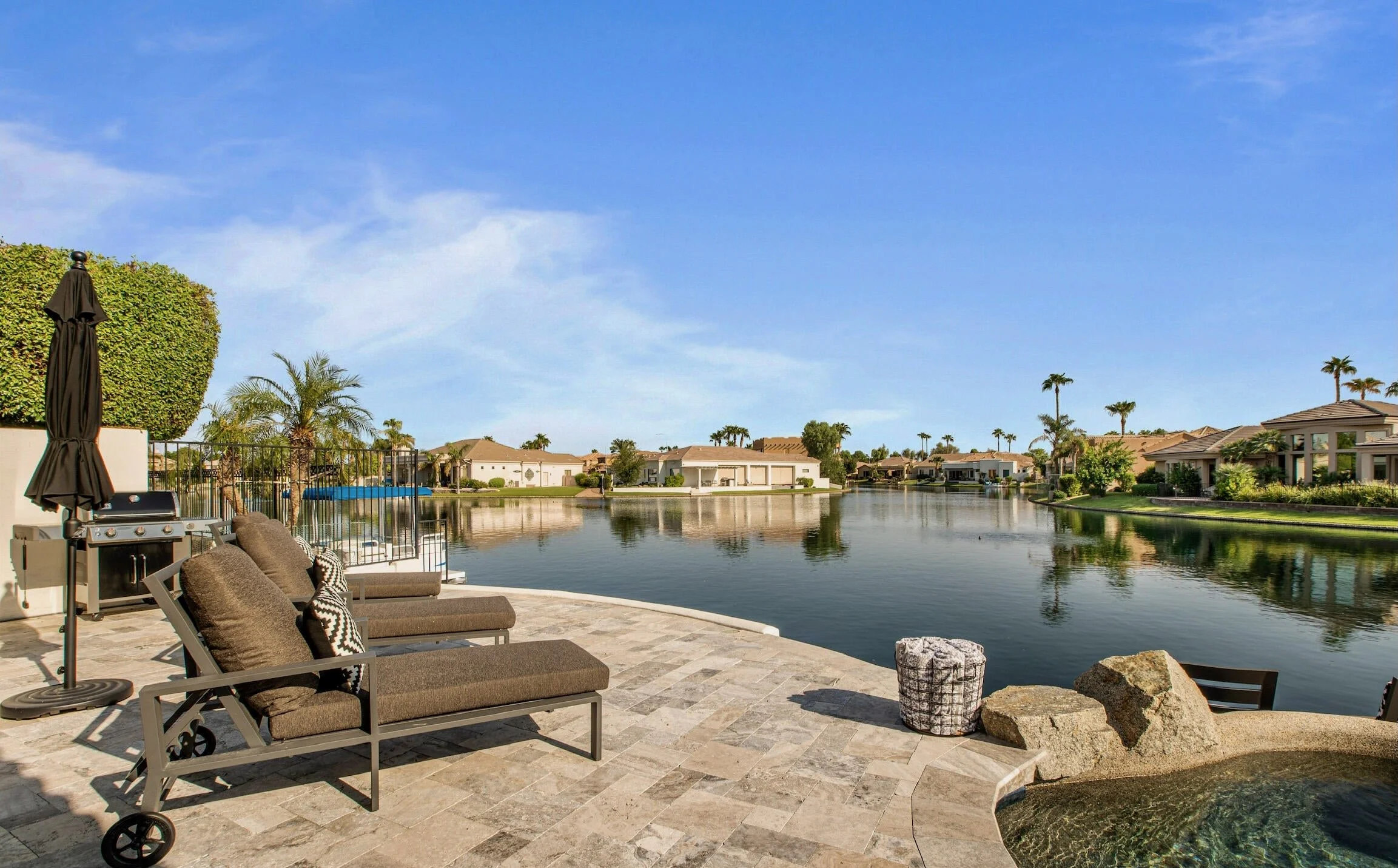 Lake view from a patio in Ocotillo, Chandler, with lounge chairs, a pool edge and homes across the water.