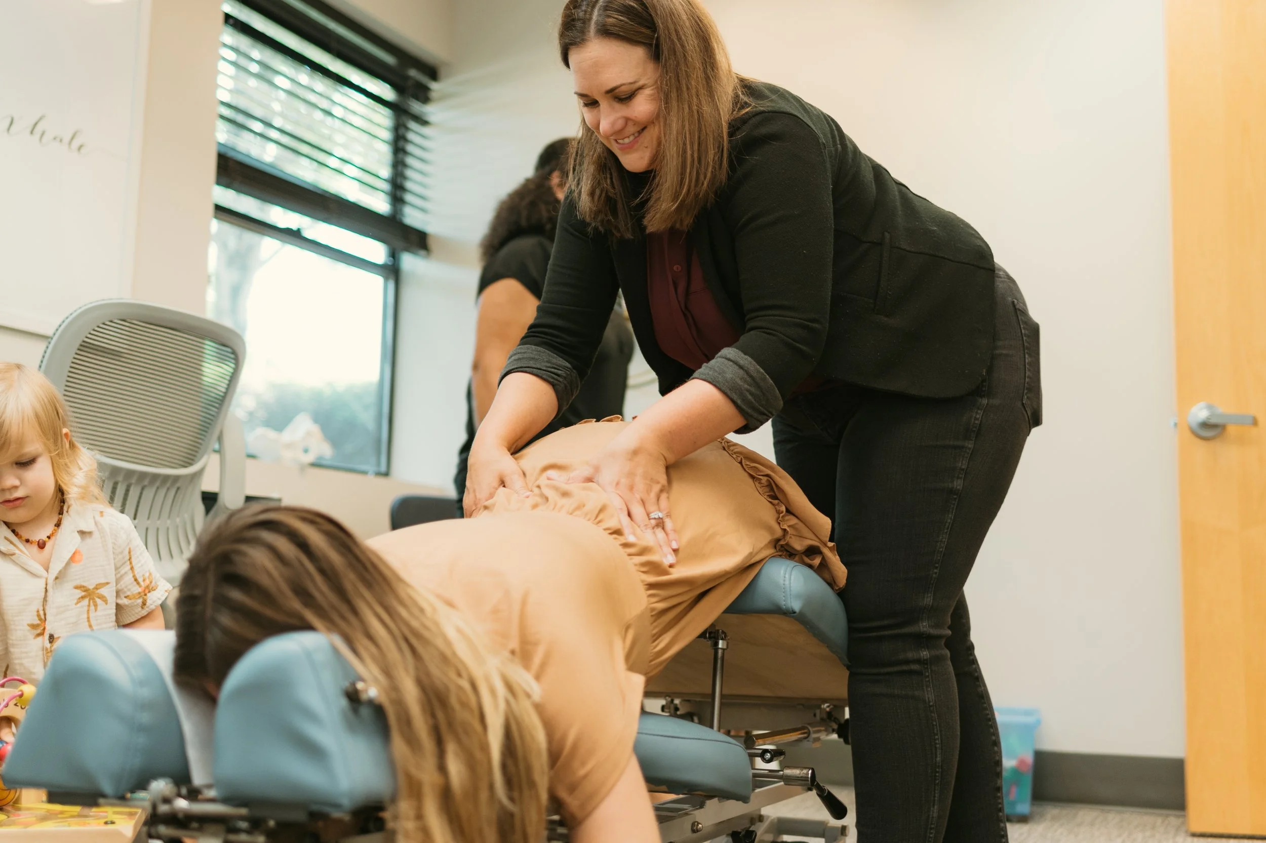 A woman giving a CPR demonstration on a mannequin in a classroom with children and other adults watching.