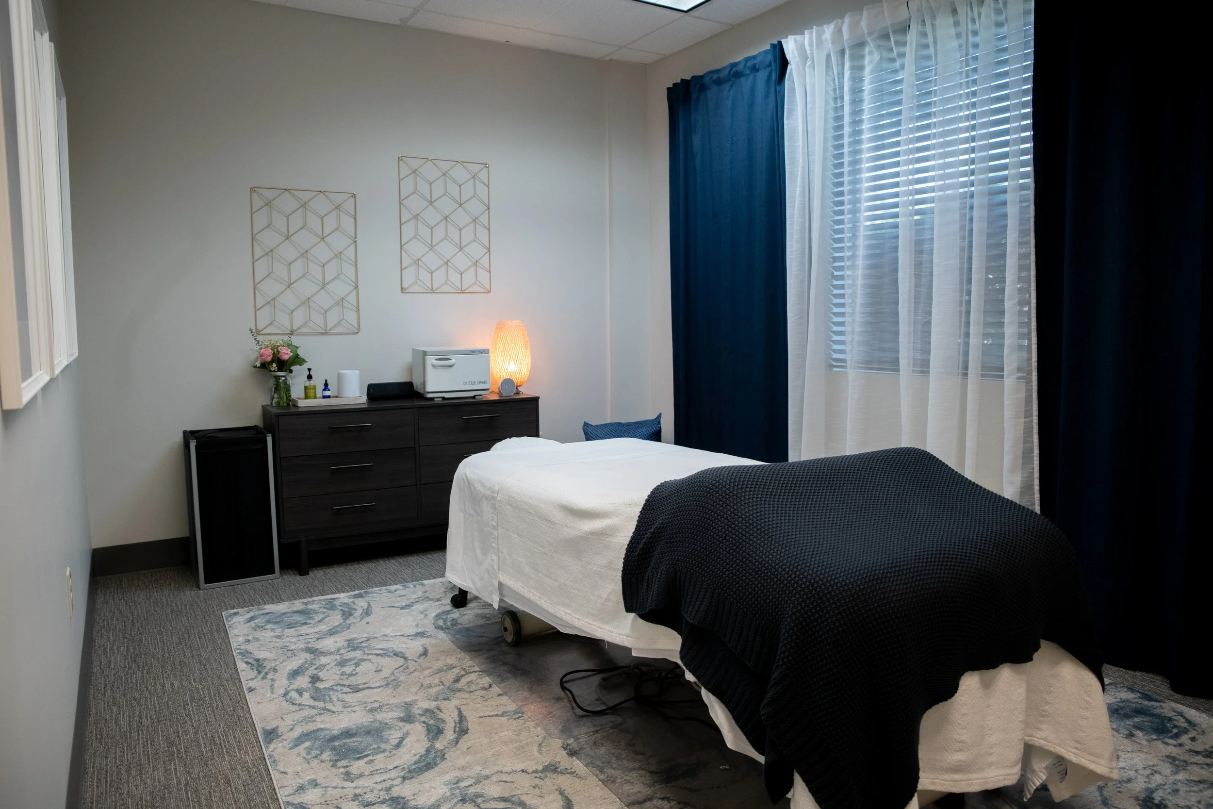 Interior of a bedroom with a bed, dresser, and window with blue and white curtains