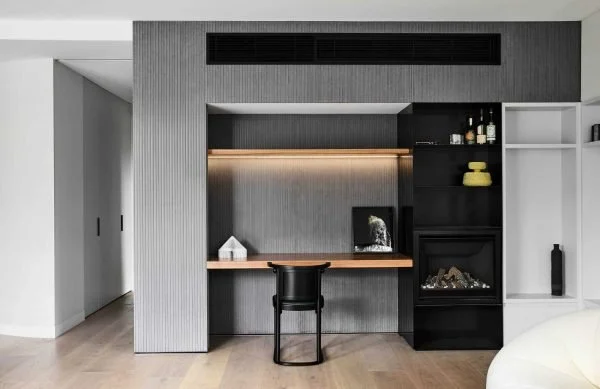 Modern interior with built-in black and gray shelving, a small desk with a black chair, and minimal decorative items including bottles and dishes, in a contemporary living space.