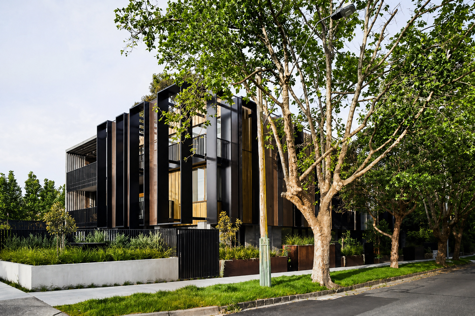 Modern residential building with wooden and black metal exterior, surrounded by trees, greenery, and a sidewalk.