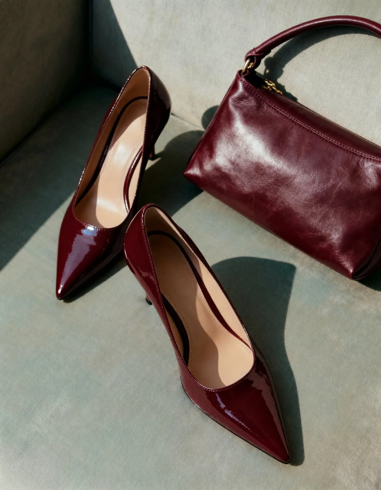A pair of shiny red high-heeled shoes and a matching red handbag on a green surface.