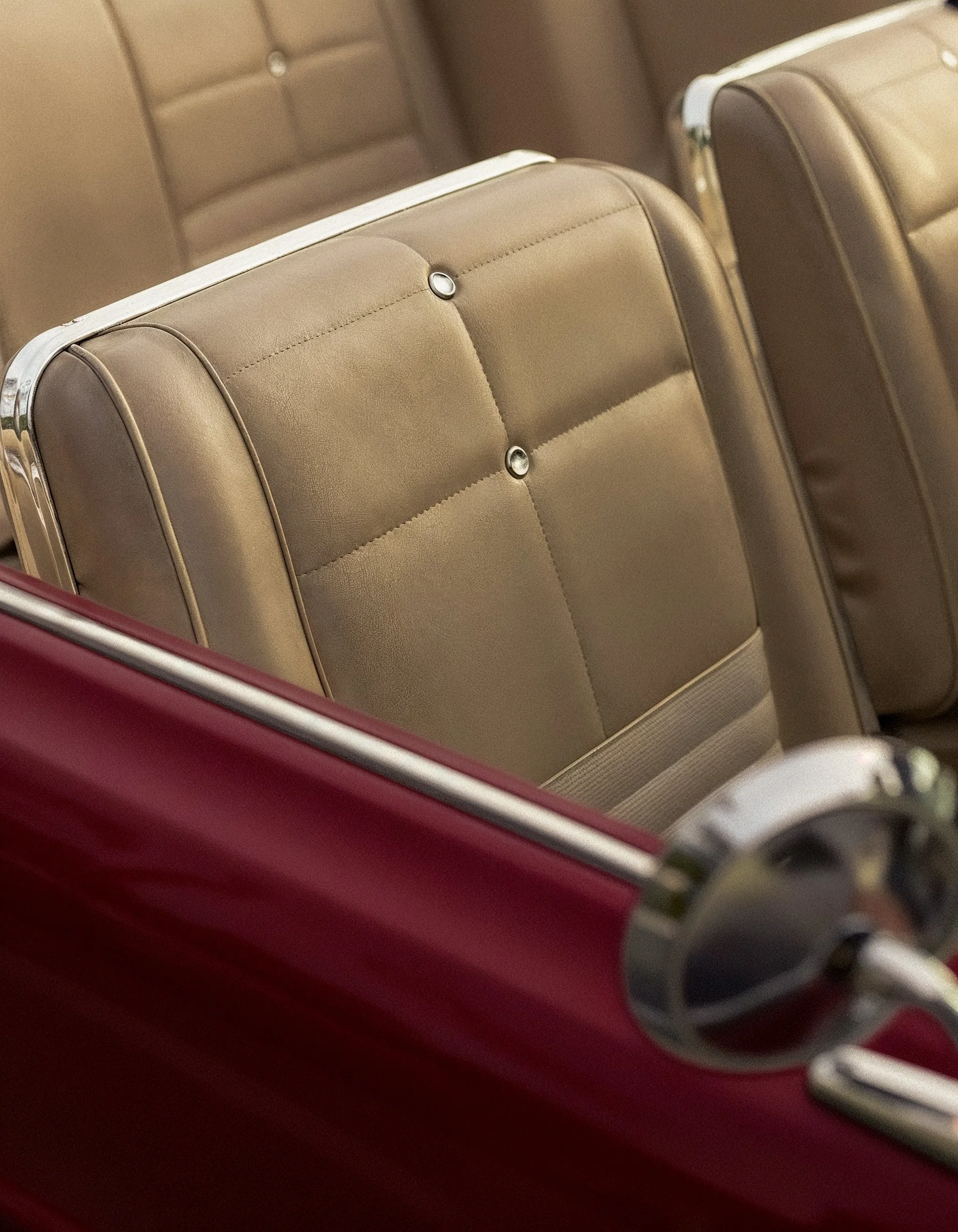Close-up of a beige vintage car seat with chrome accents and button tufting, part of a classic car interior.