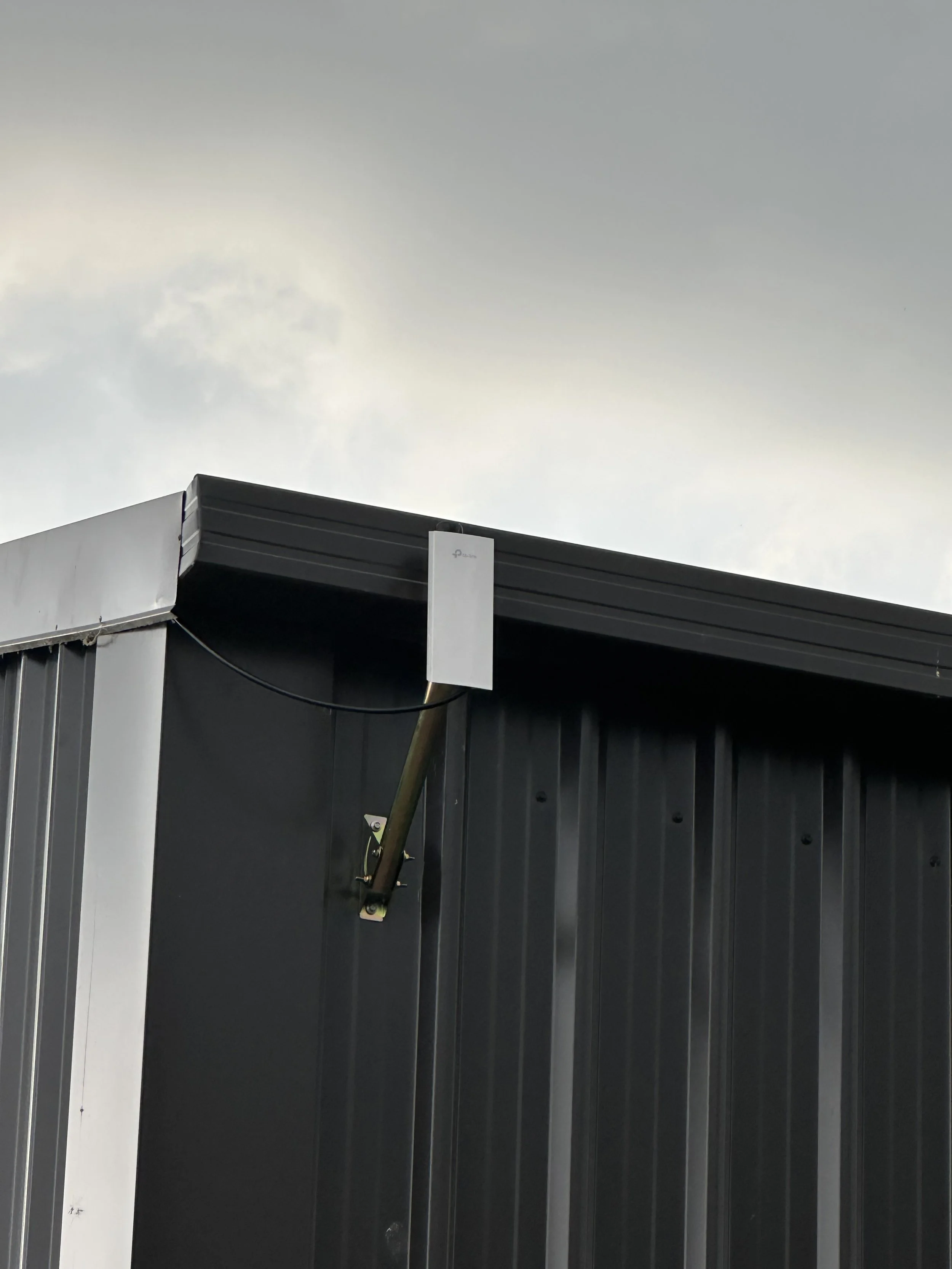 A white device mounted on the corner of a building with a metal exterior against a cloudy sky.