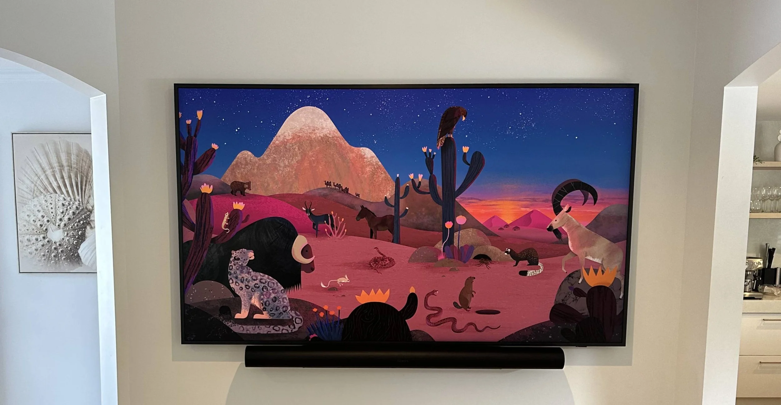 Colorful desert landscape artwork displayed on a wall, featuring various animals and cactus under a starry sky.