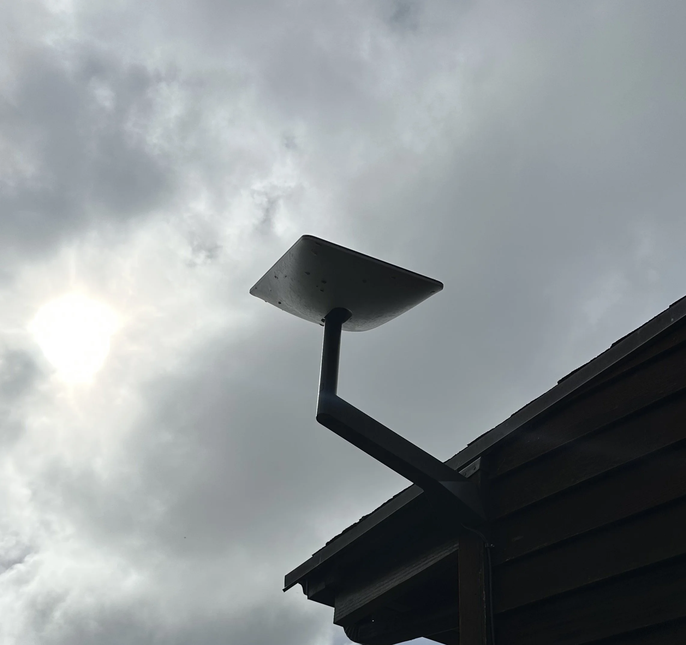 Outdoor security or floodlight mounted on the roof of a building against cloudy sky.