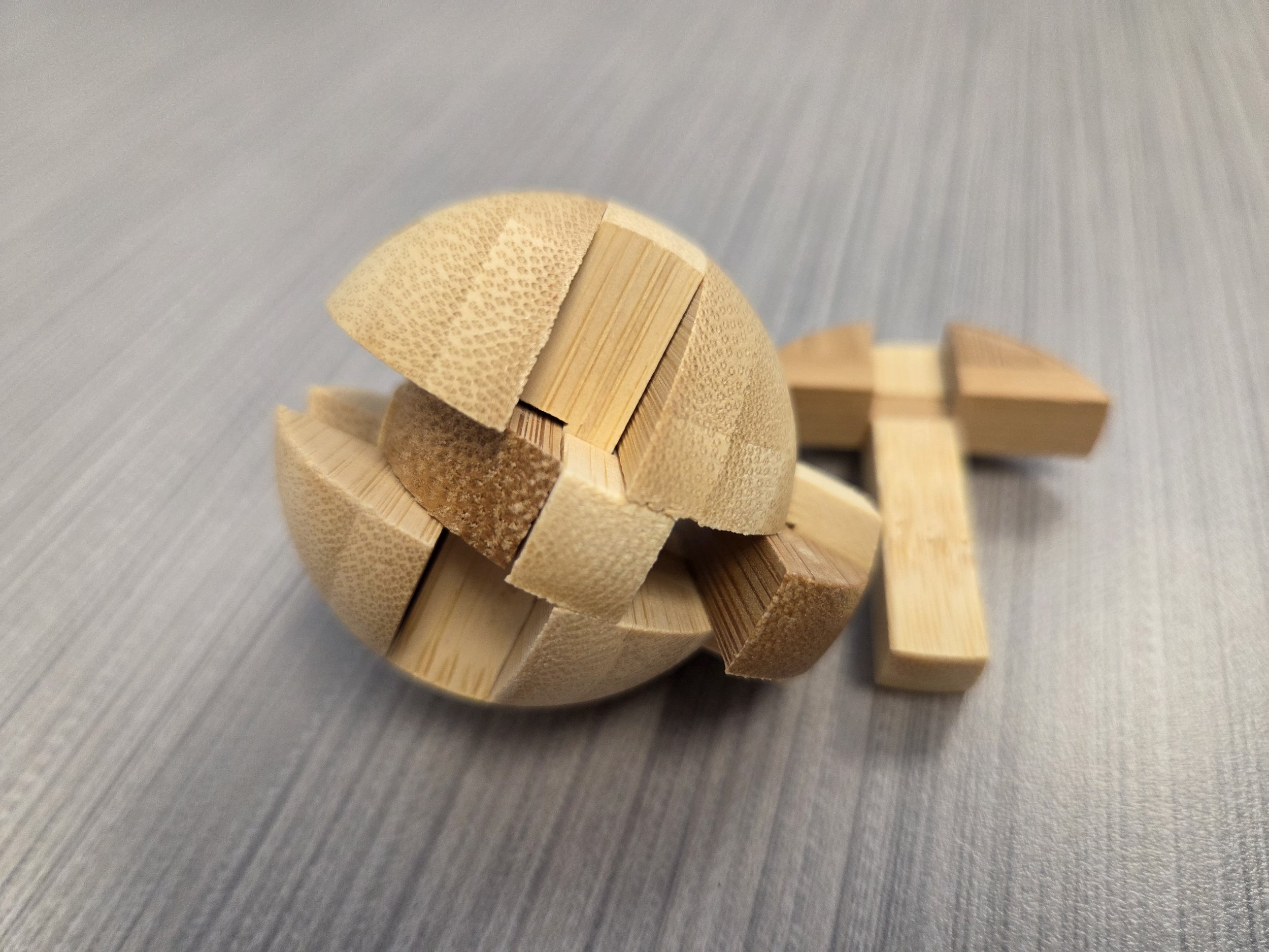 A disassembled wooden interlocking sphere puzzle on a textured surface, illustrating the logic and brain teasers included in the subscription.