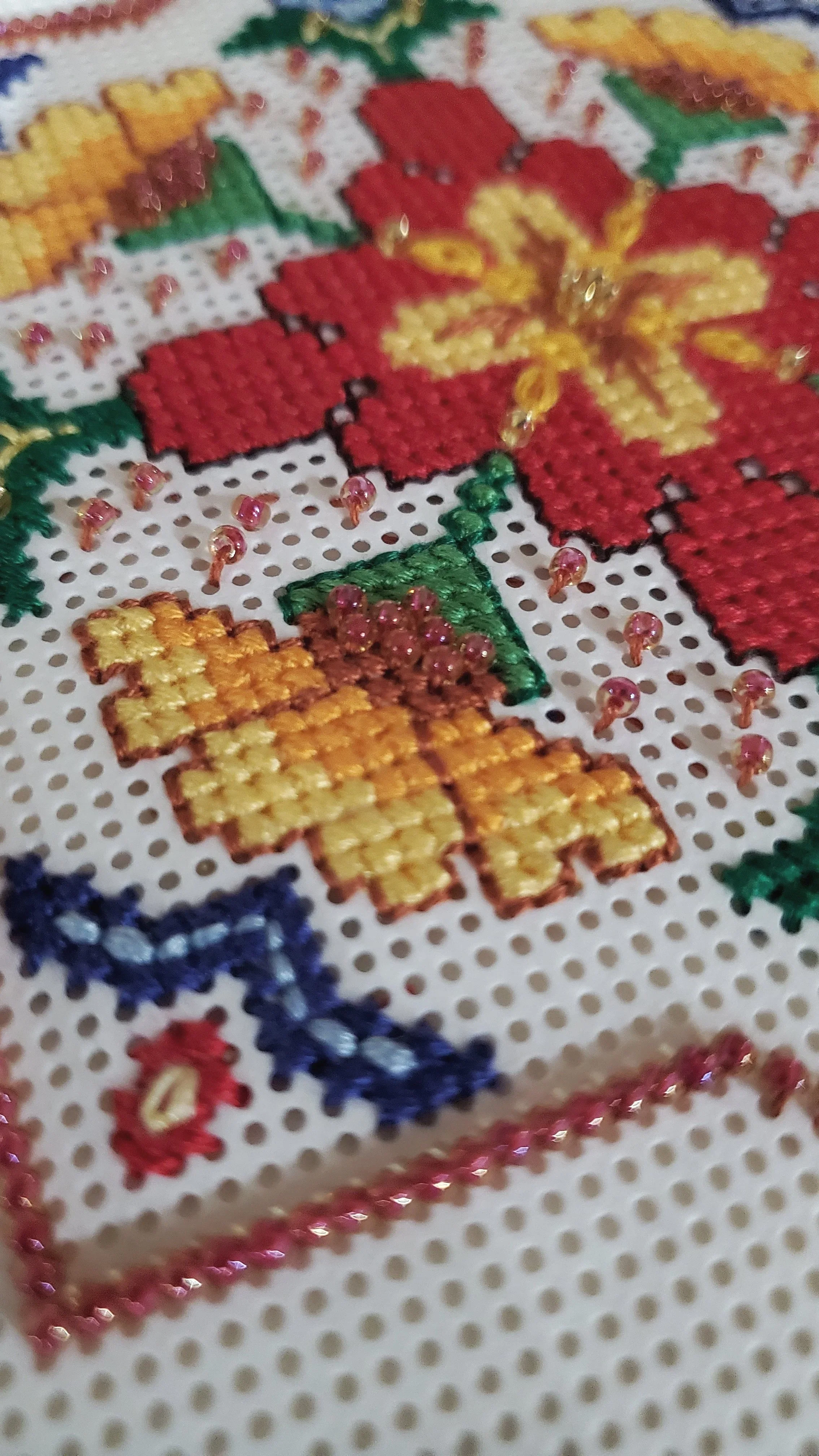 A macro photograph of colorful cross-stitch and beadwork on a white canvas, representing the artisanal hand-work featured in Post & Petal stories.