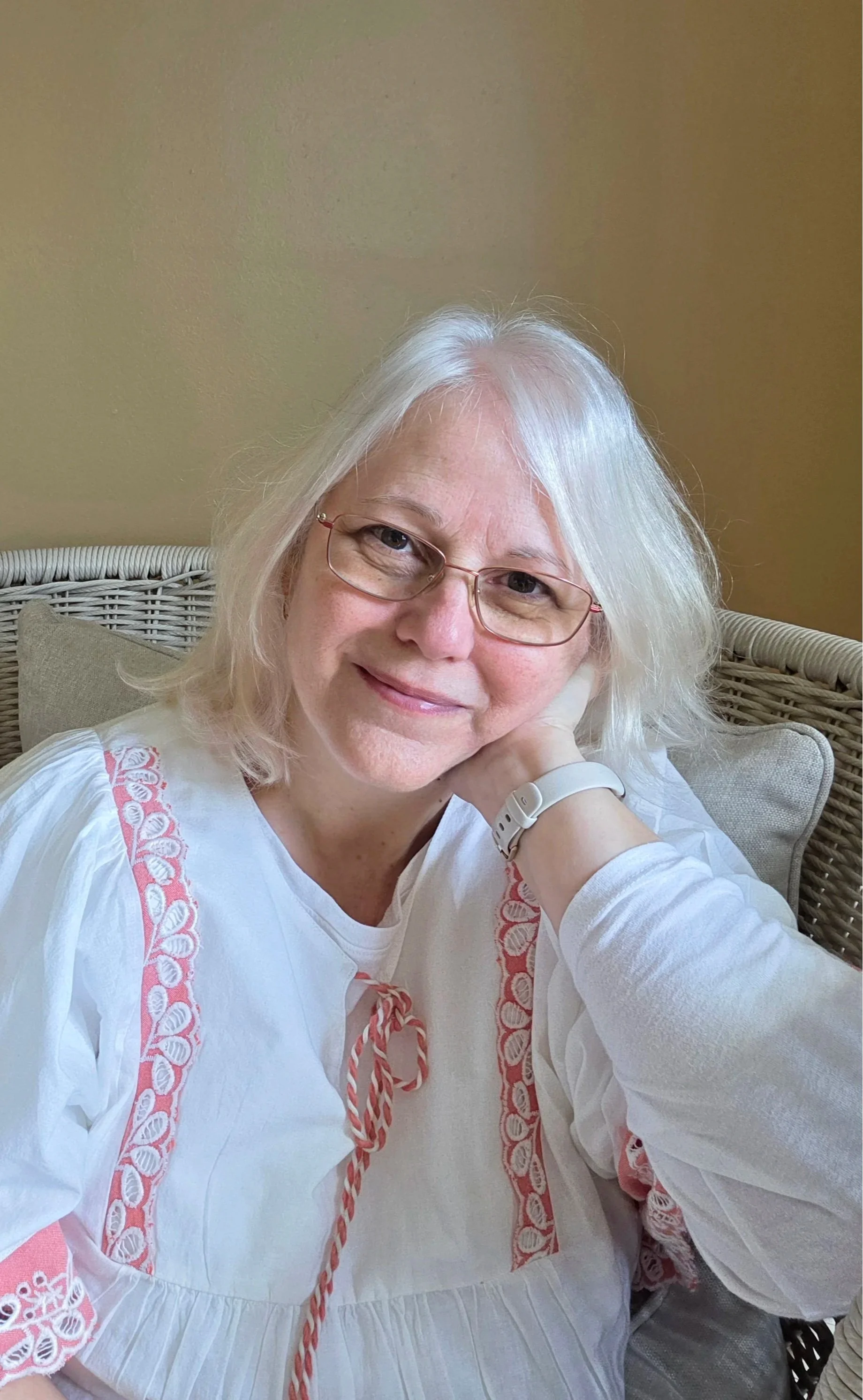 Portrait of the founder of Post & Petal, a woman with silver hair and glasses wearing a white embroidered blouse, representing the personal and handcrafted nature of the Monthly Folio.