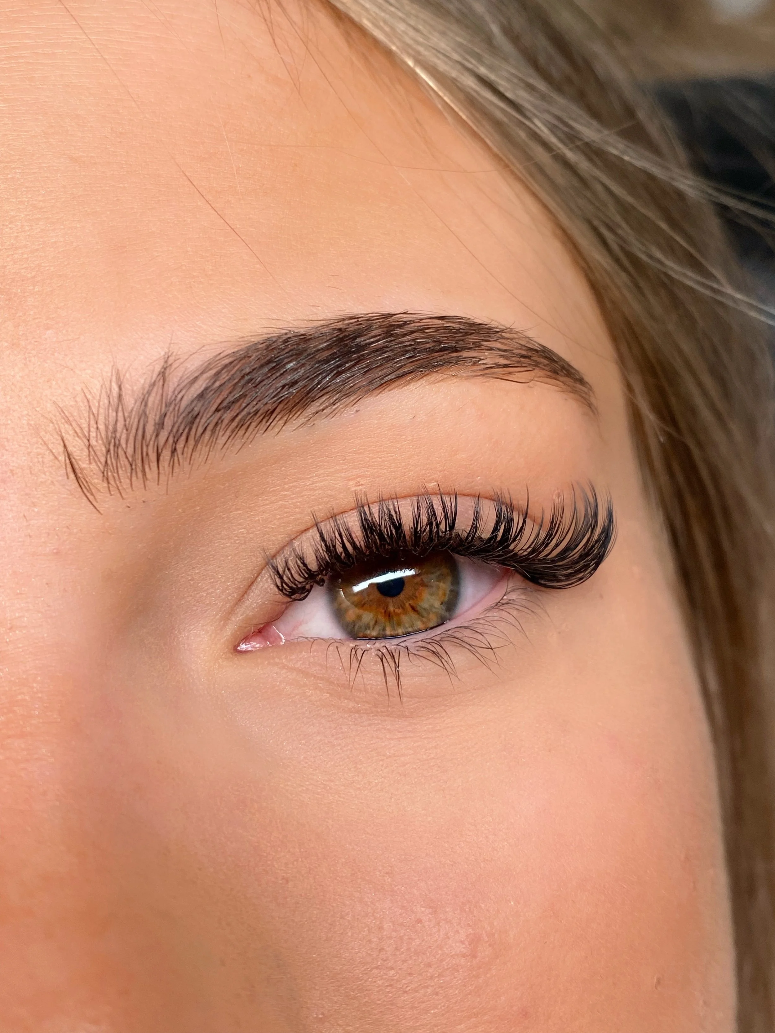 Close-up of a person's eye with long eyelashes, brown iris, and well-groomed eyebrow.