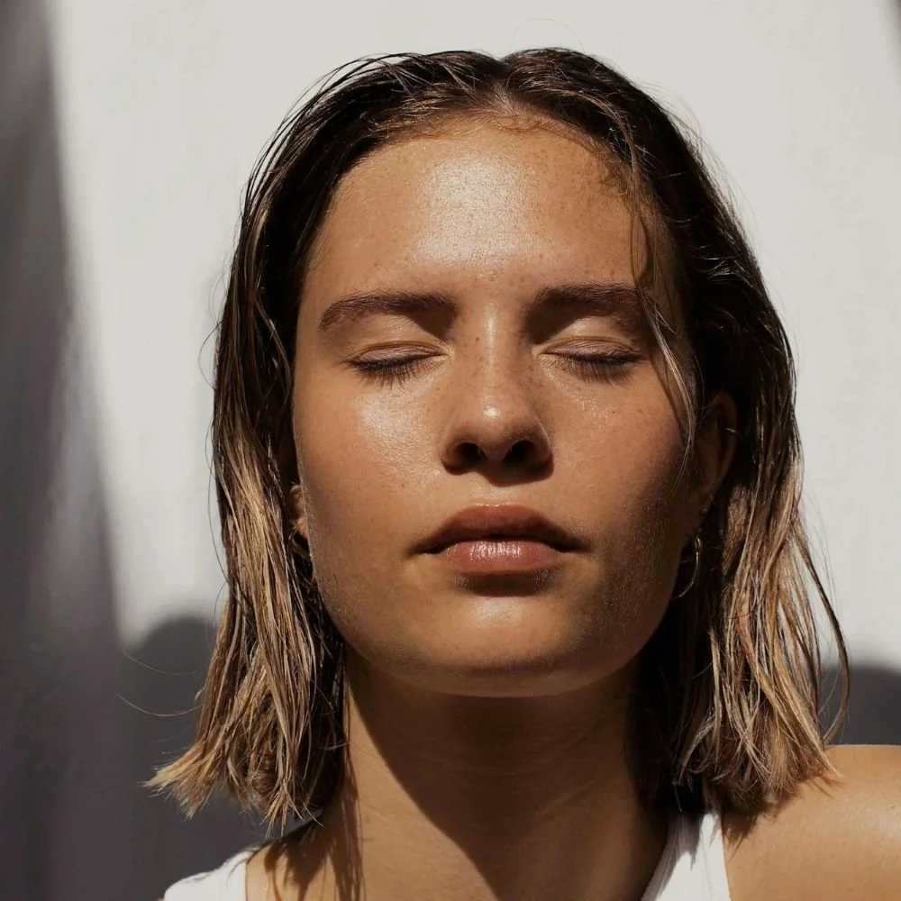 Close-up of a woman with wet hair and closed eyes, sunlight on her face.