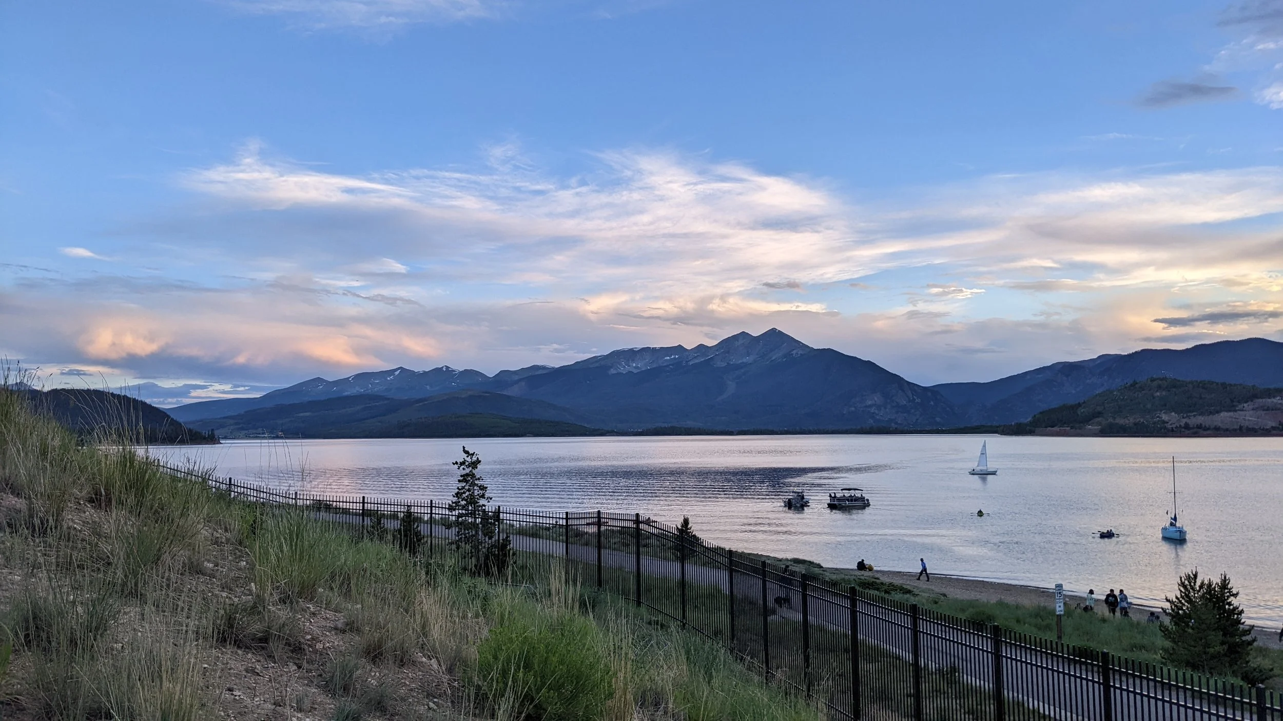 Lake Dillon with boats, surrounded by mountains and a partly cloudy sky at sunset.