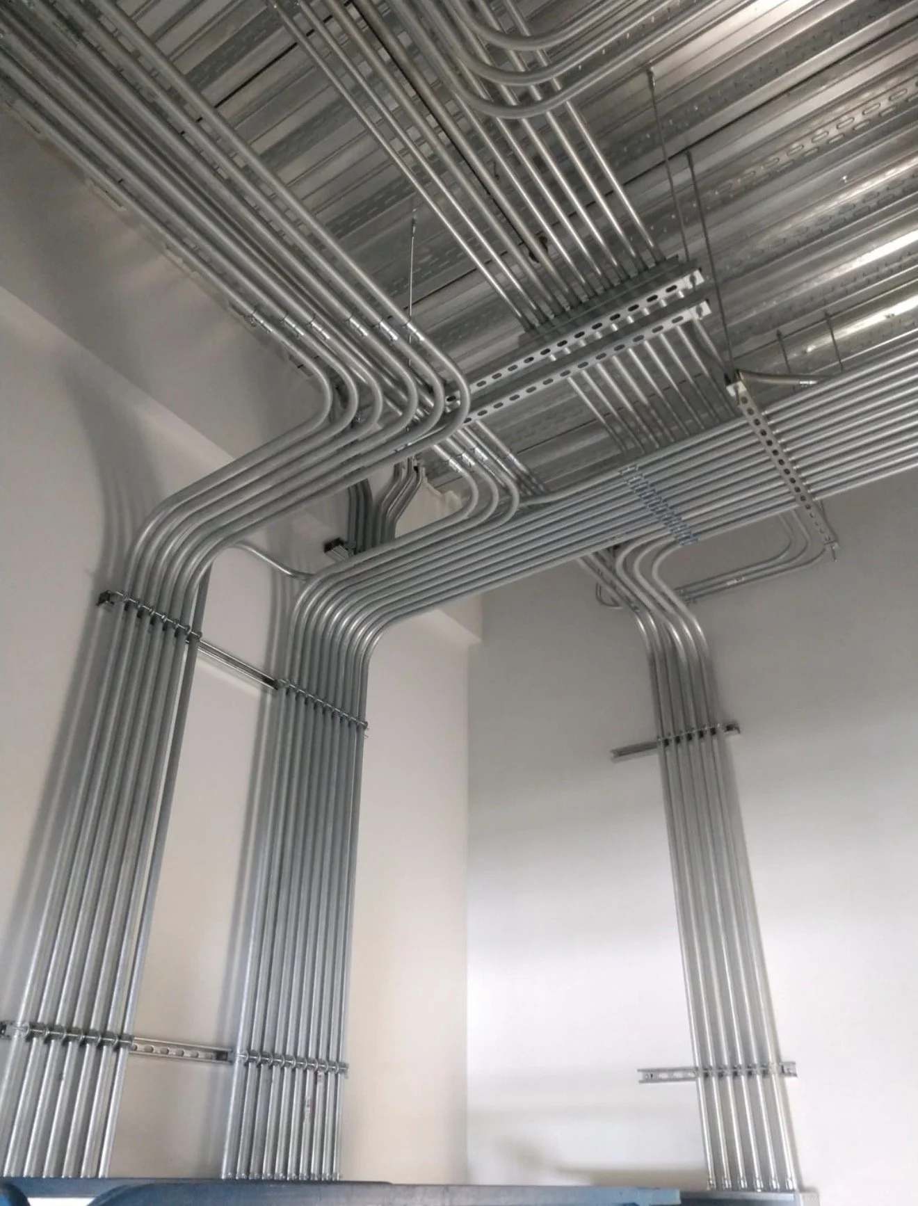 Metal electrical conduit pipes installed on a ceiling and walls in a building under construction.
