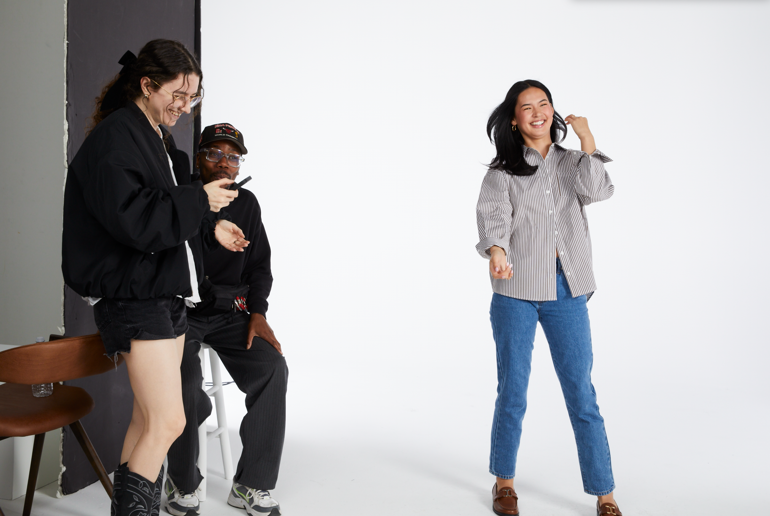 Group of people posing in a photography studio with a white background, including a woman smiling and adjusting her hair, and others sitting or standing nearby.