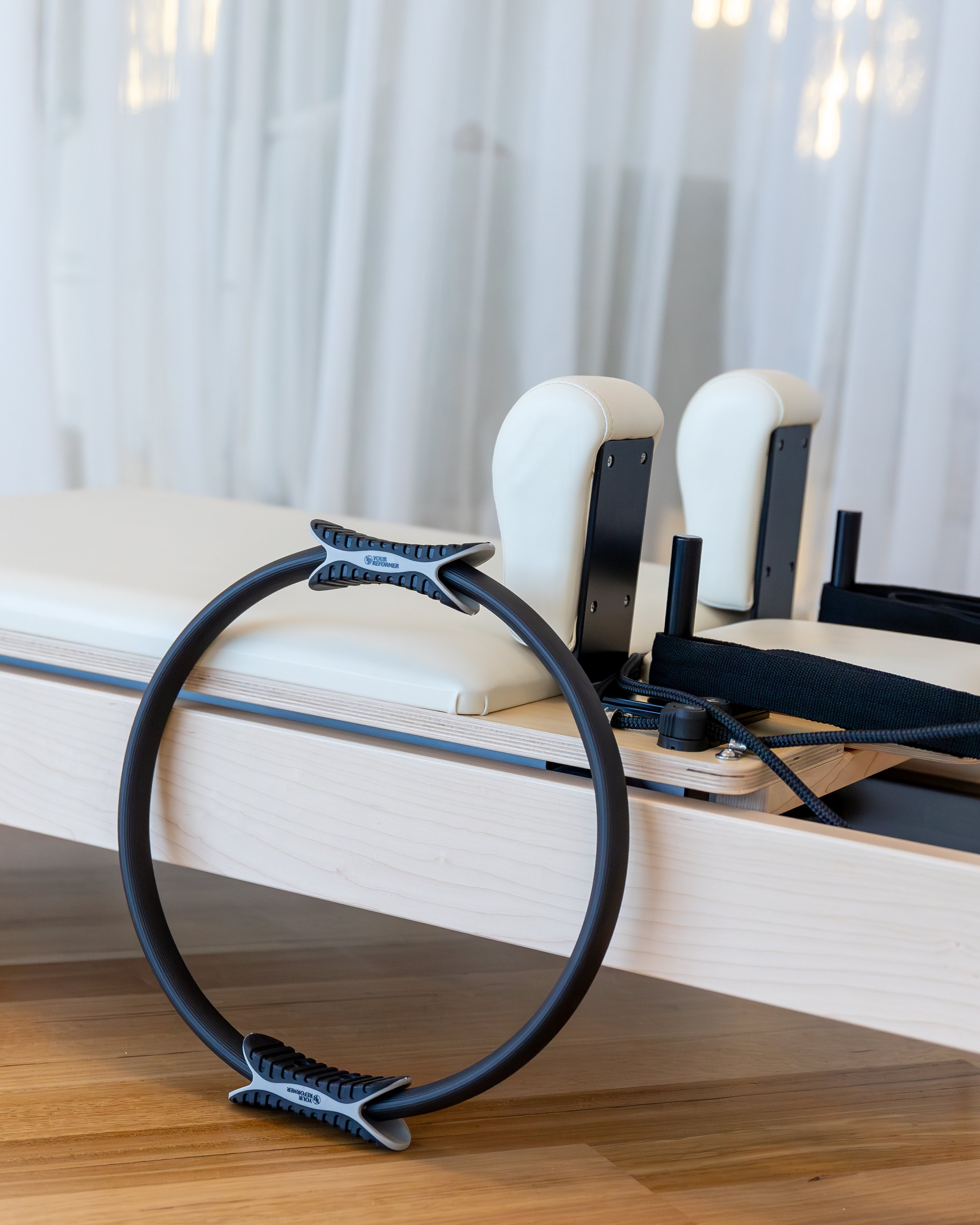 A pair of black and gray resistance band exercise equipment sitting in front of a white table with white chairs against a white wall with vertical blinds