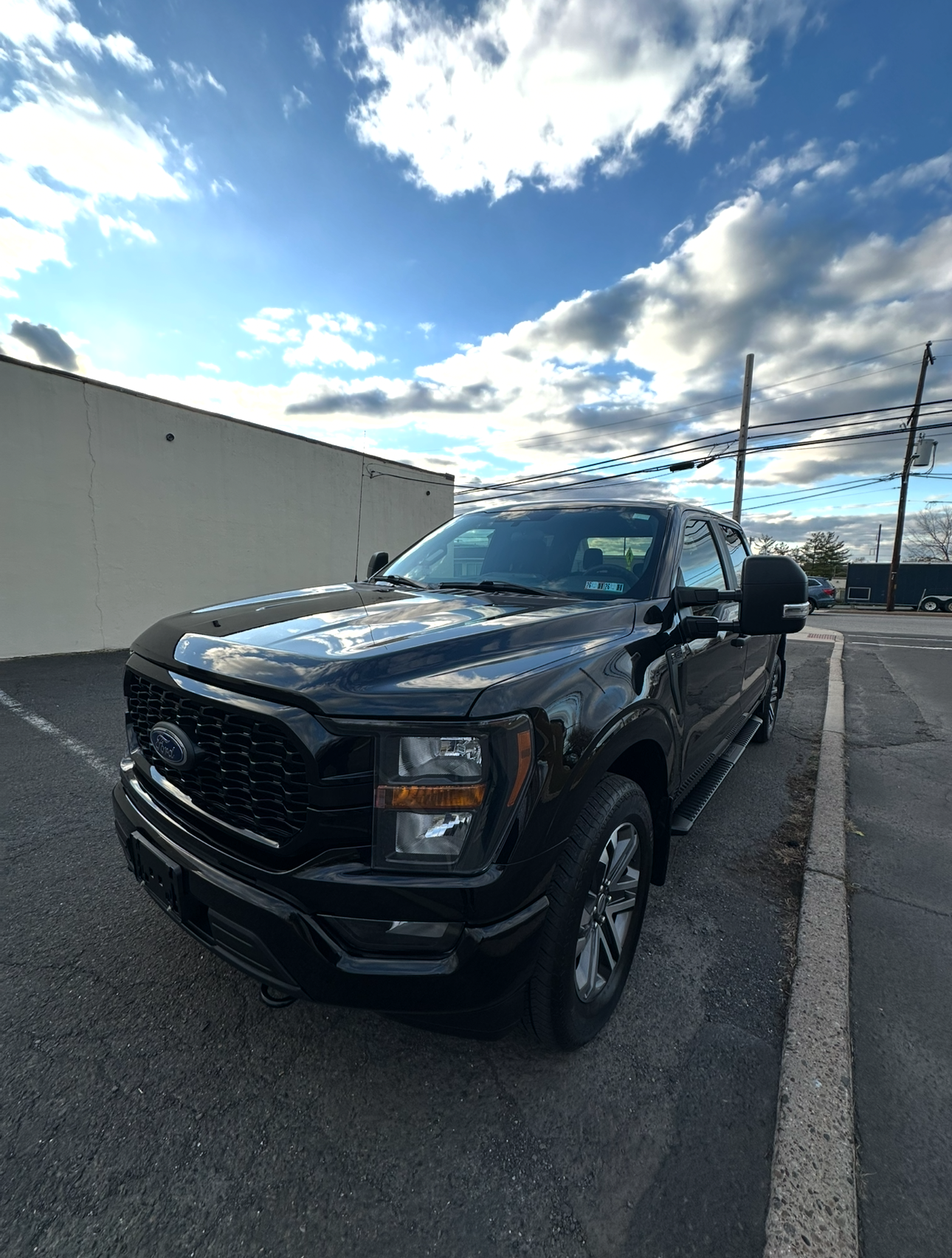 Black Ford pickup truck parked on the street under a partly cloudy sky.
