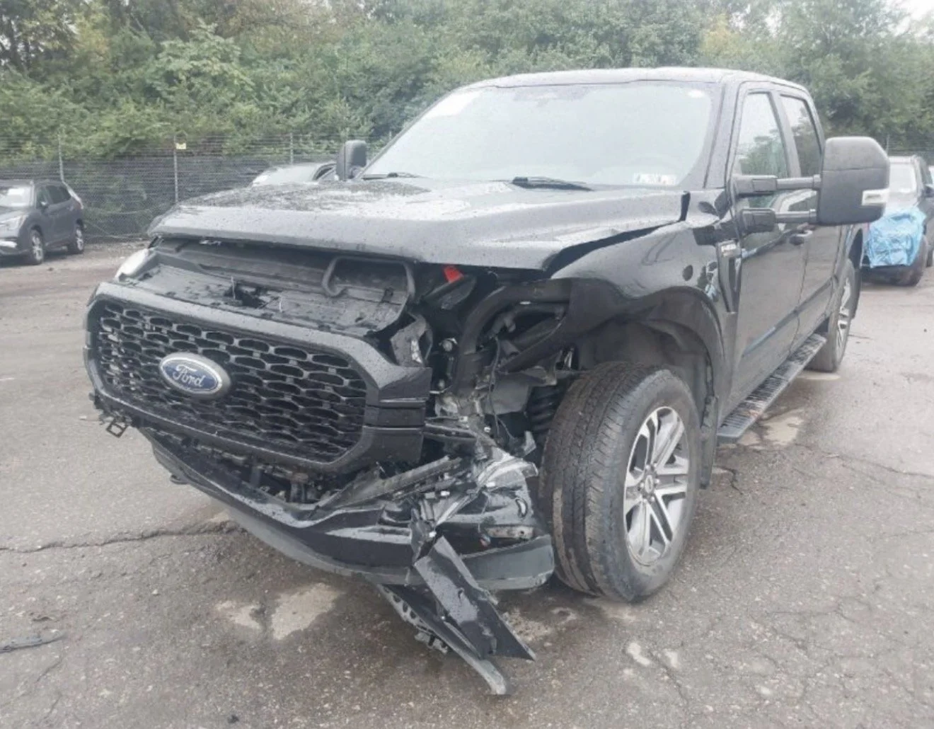 A black Ford pickup truck with extensive front-end damage from a collision, parked on a dirt lot.