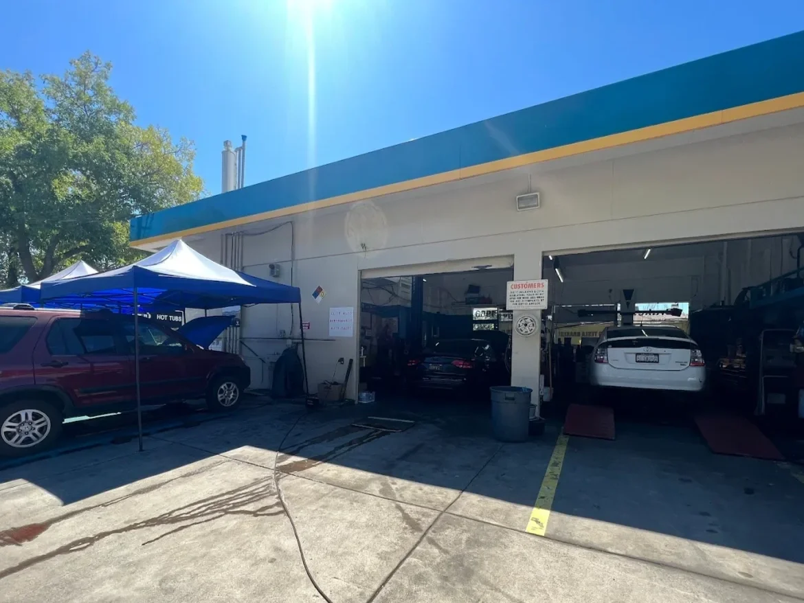 Car wash station with cars being washed inside and outside, blue tents set up outside, and sunny weather.
