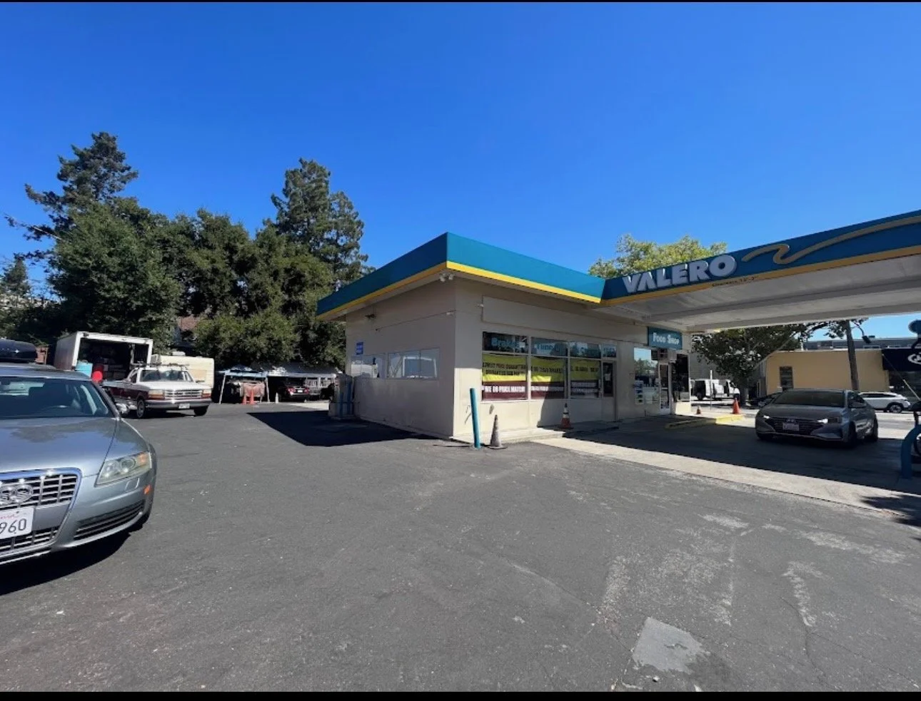 A Valero gas station with a blue and yellow canopy, gas pumps, and parked cars under a clear blue sky.