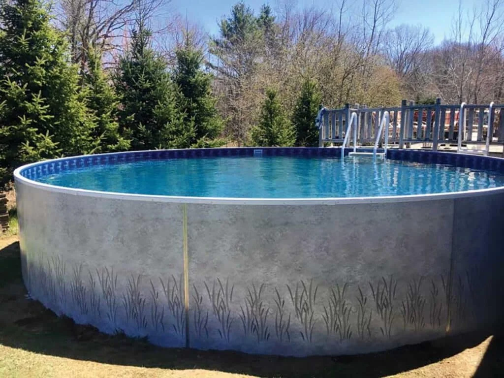 Circular above-ground swimming pool with ladder, surrounded by trees and a wooden deck railing in the yard.