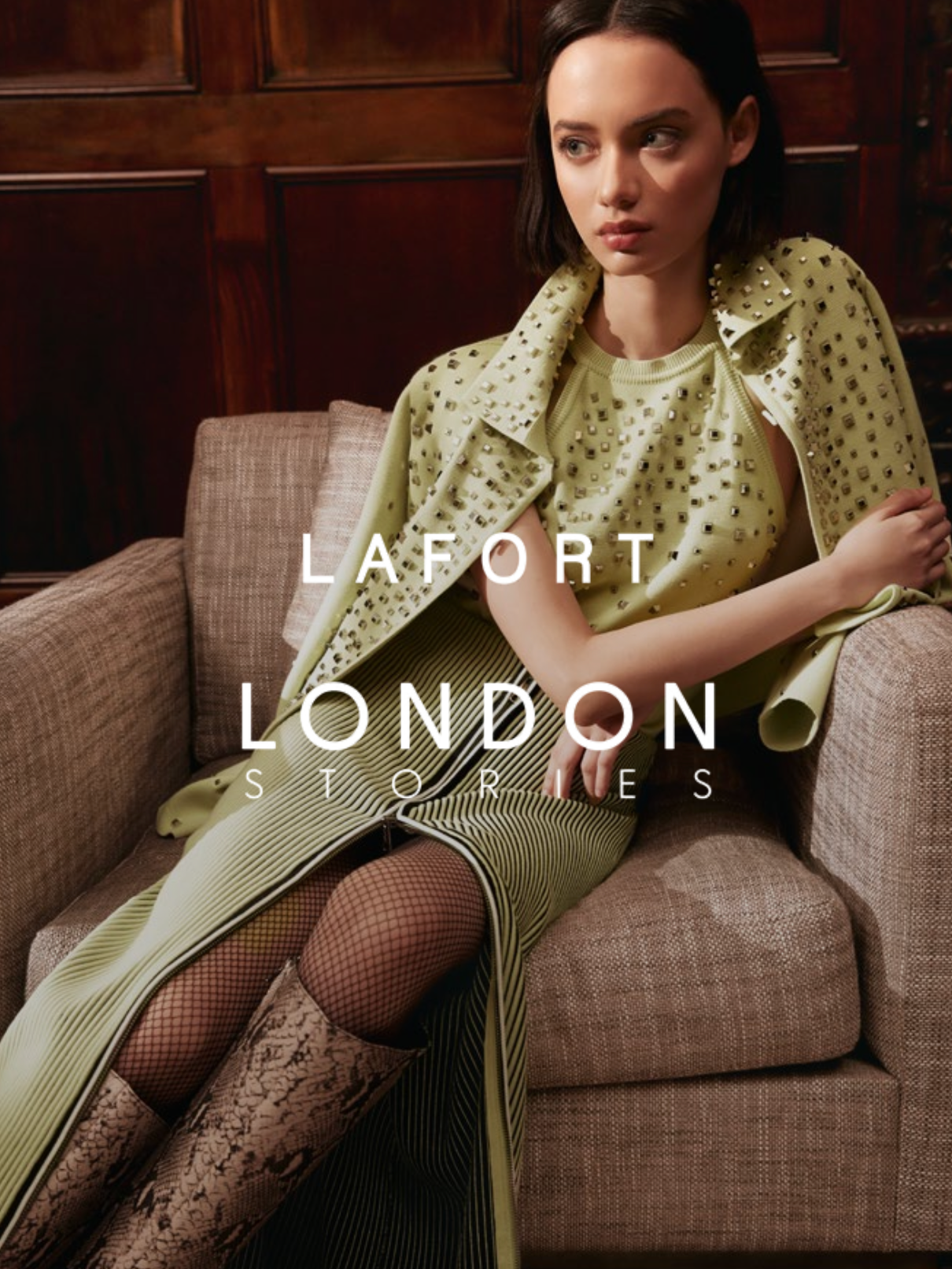 Mulher jovem sentada em um sofá de tecido, vestindo roupas de moda com detalhes de vestuário de alta costura, para uma campanha da loja LaFort London Stories.