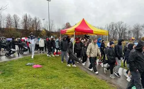 Long line of people waiting outdoors near a red and yellow tent on a cloudy day.