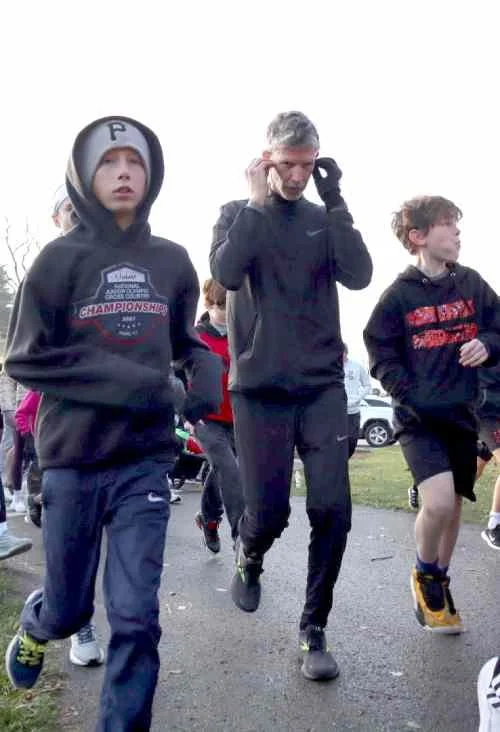 Group of children and an adult jogging outdoors on a cloudy day.